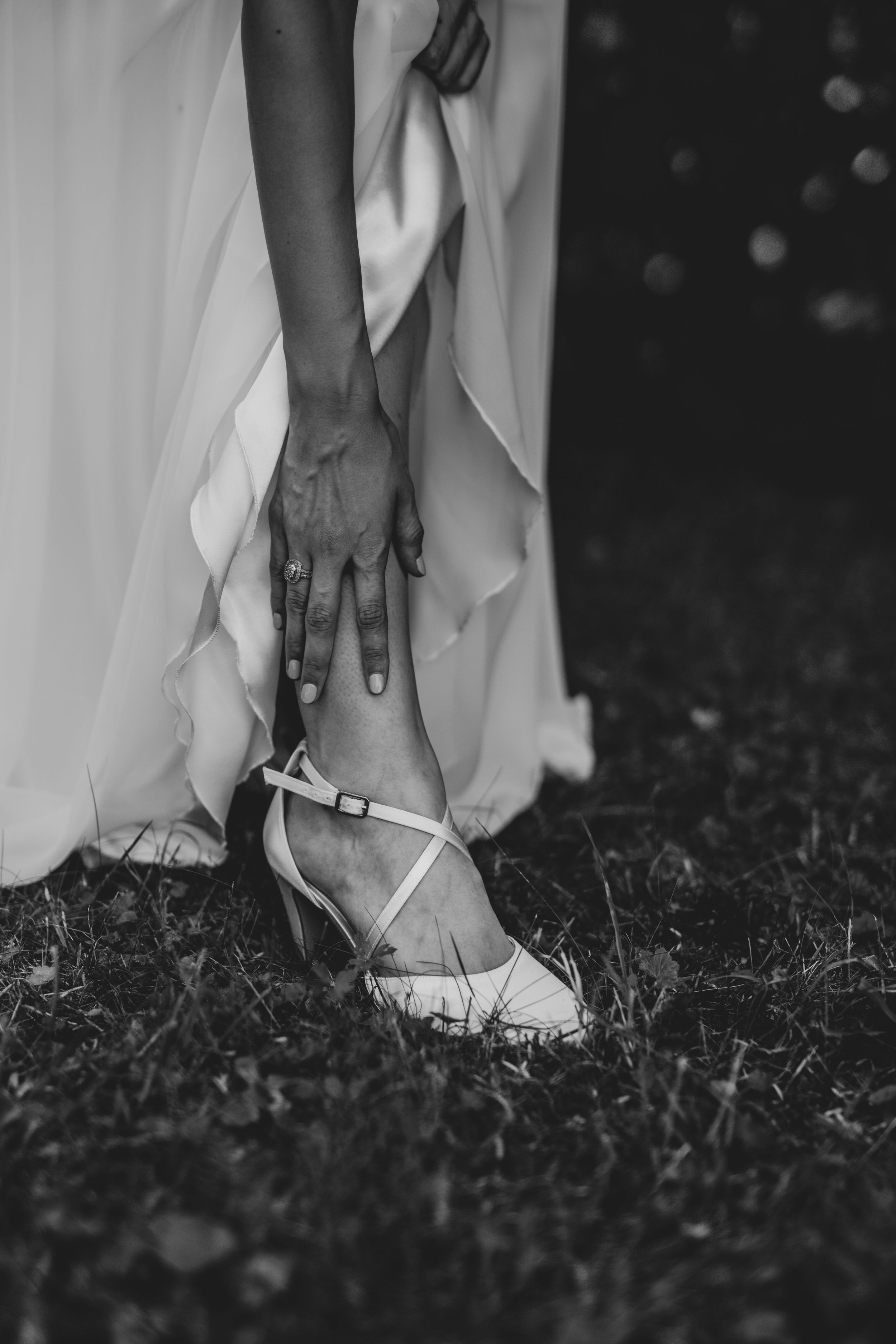 Black and white detail shot of a bride's hand adjusting her white wedding shoe strap.