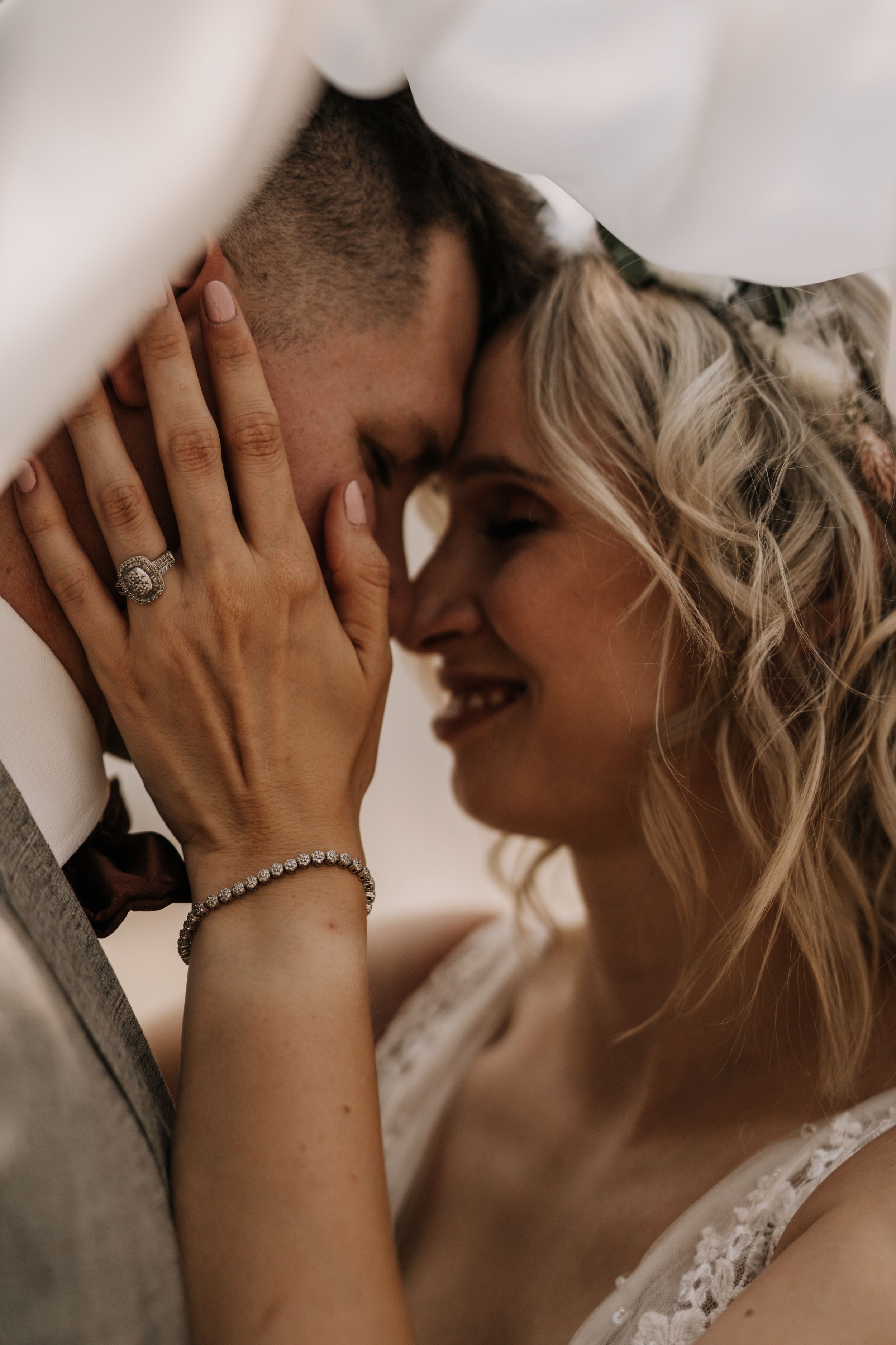 Intimate wedding portrait showing tender moment under veil with engagement ring visible.