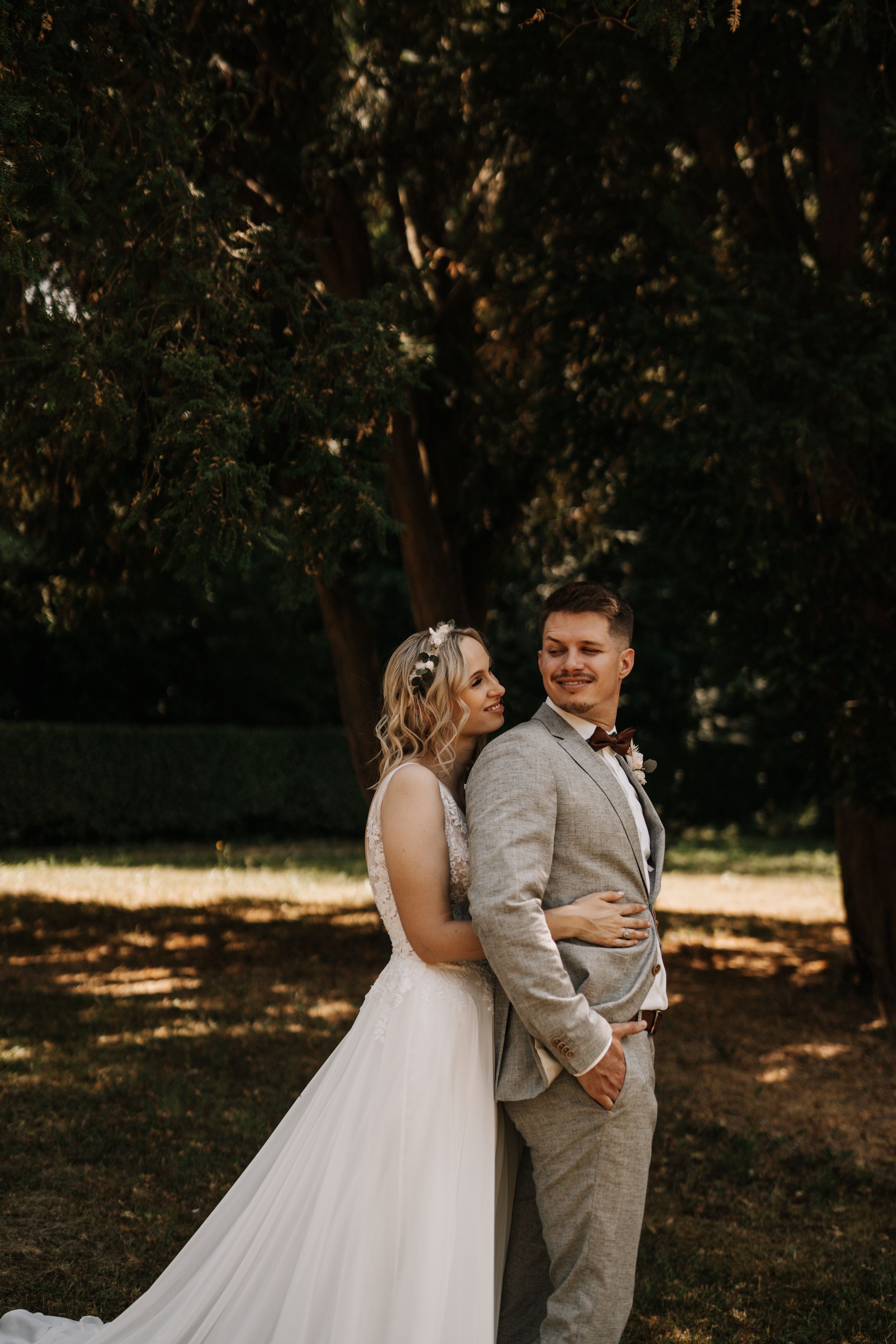 Artistic wedding portrait of newlyweds in warm sunlight against autumn trees.