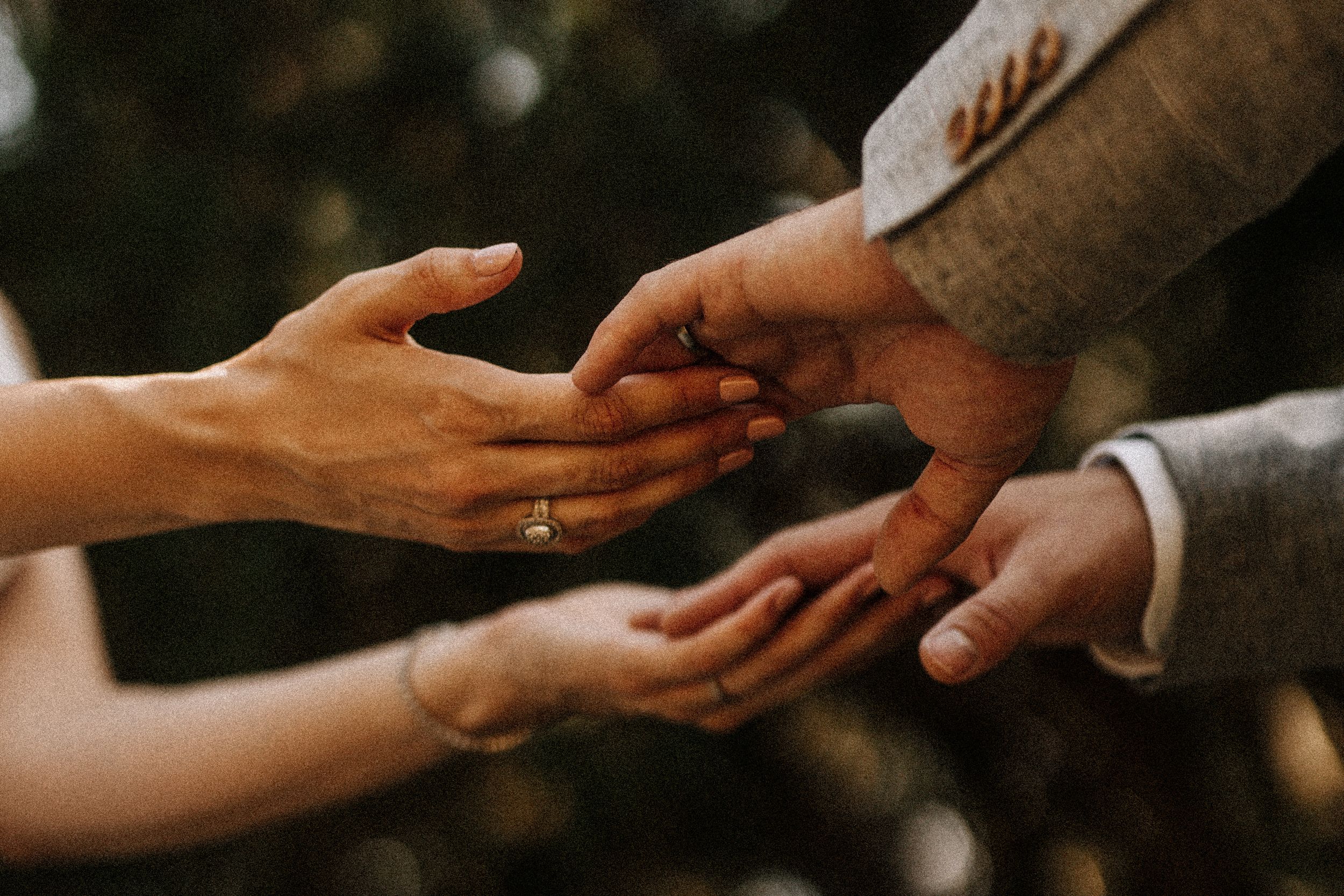 Artistic close-up of hands exchanging rings during wedding ceremony.