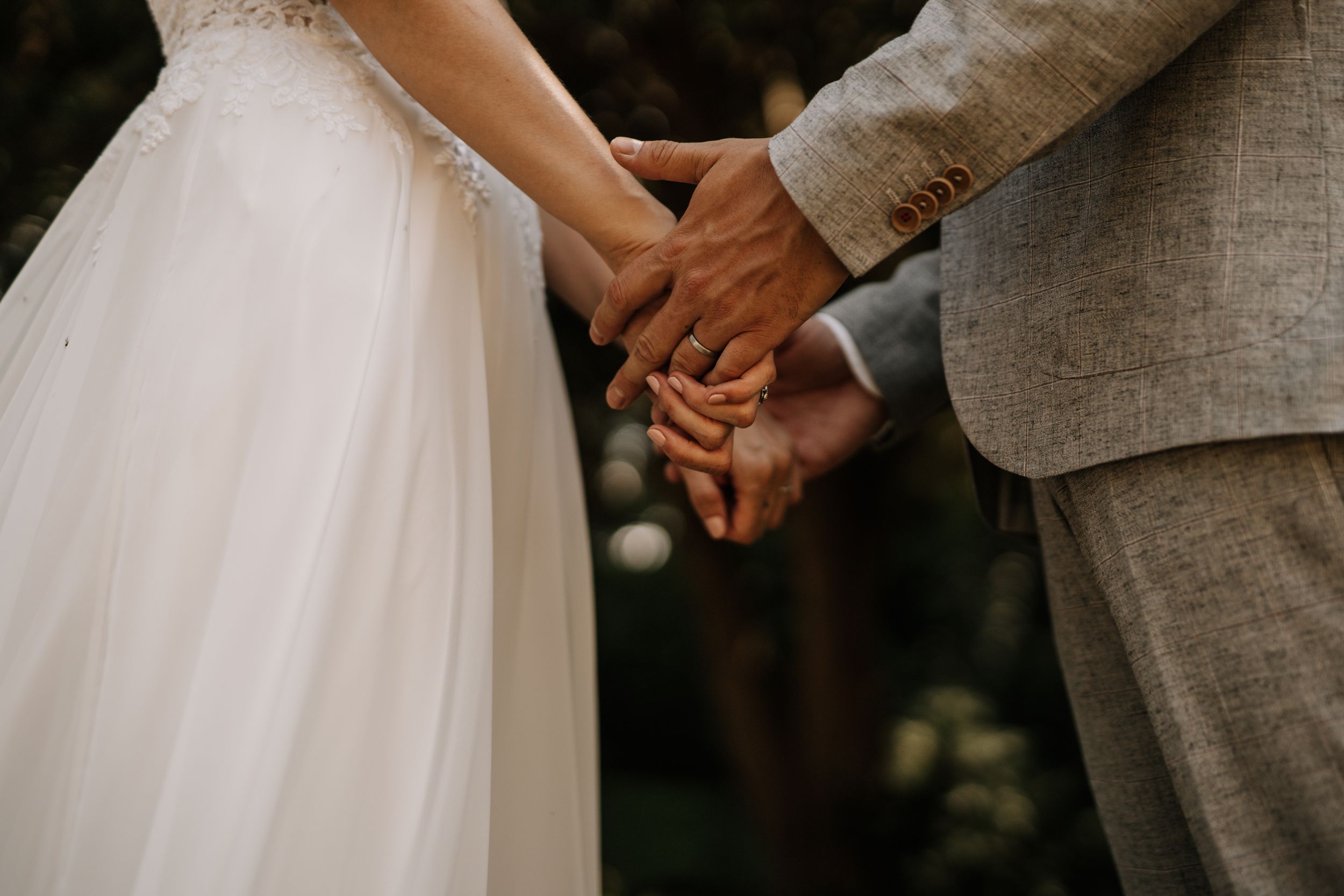 Intimate detail shot of newlyweds holding hands with wedding attire visible.