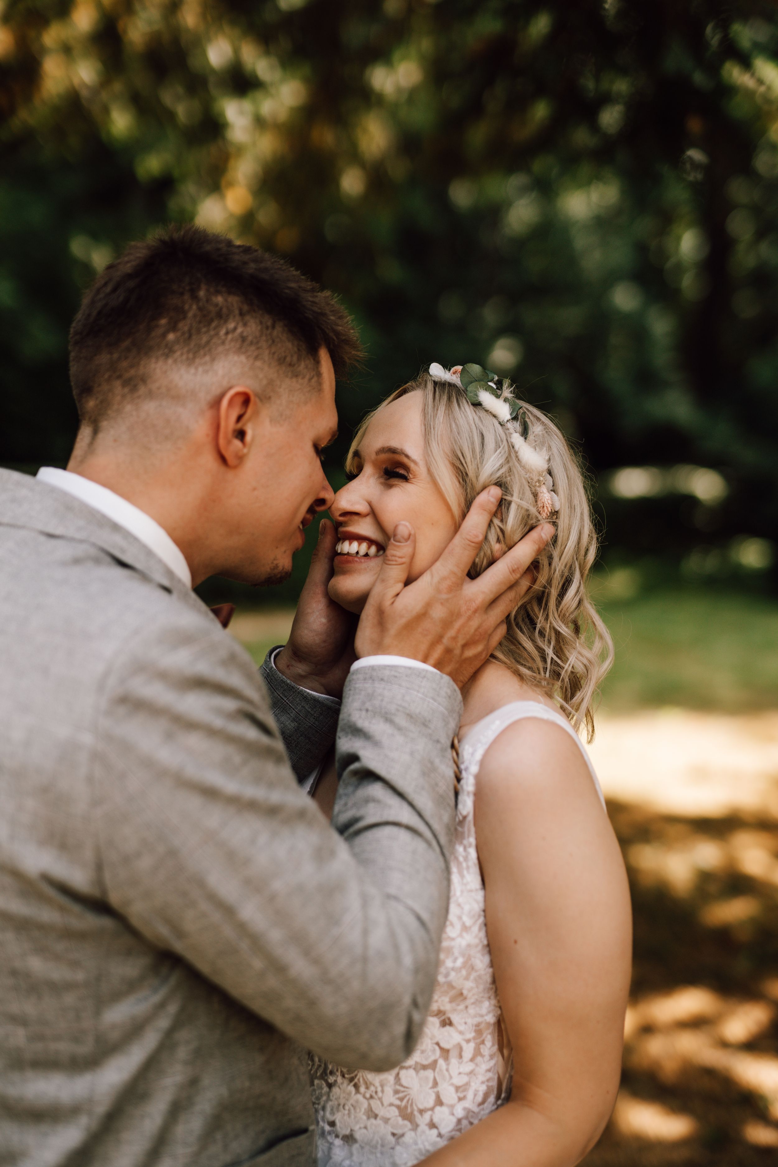 Romantic wedding couple shares intimate moments in a sun-dappled outdoor setting.