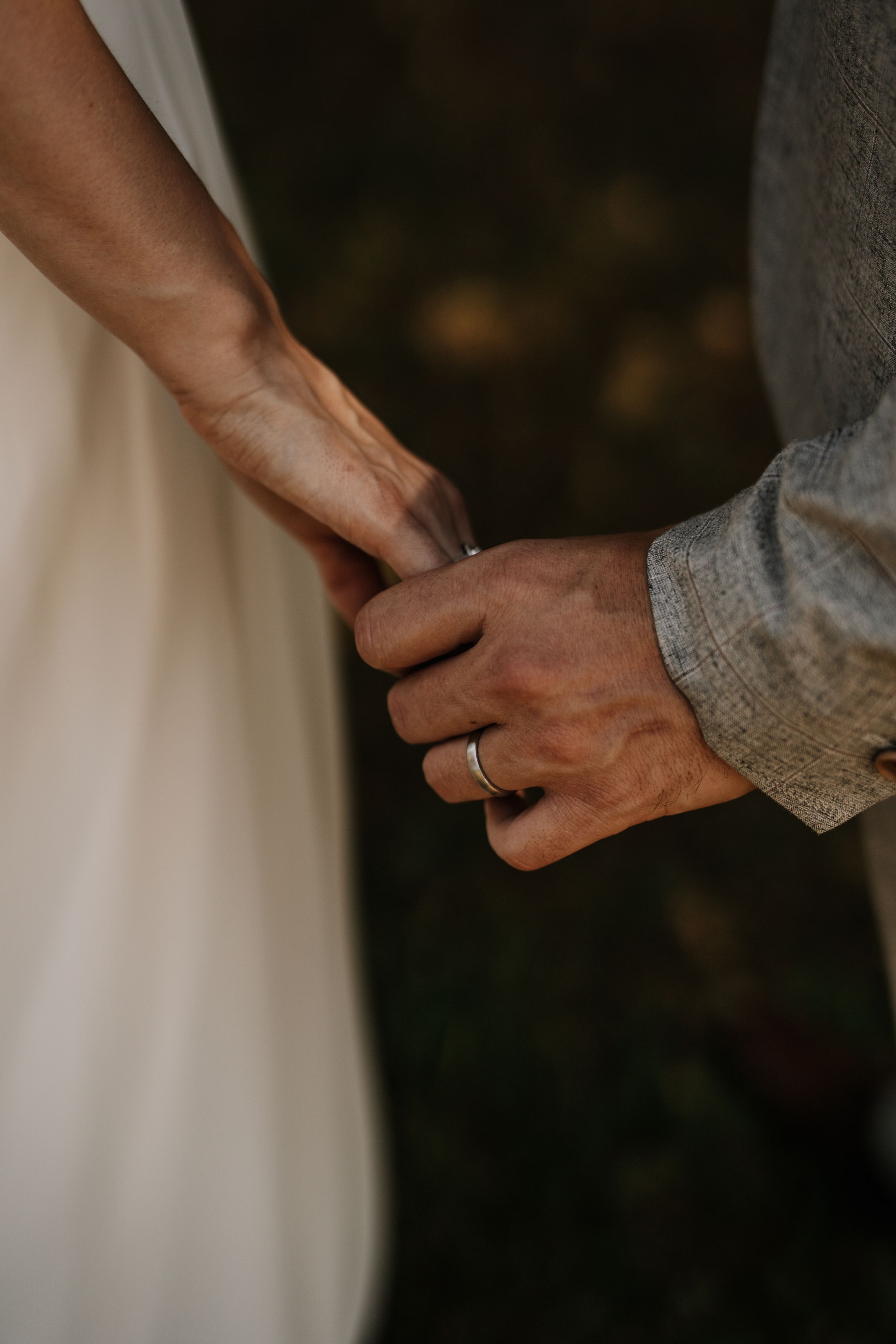 Close-up of hands holding with a wedding ring visible in soft lighting.