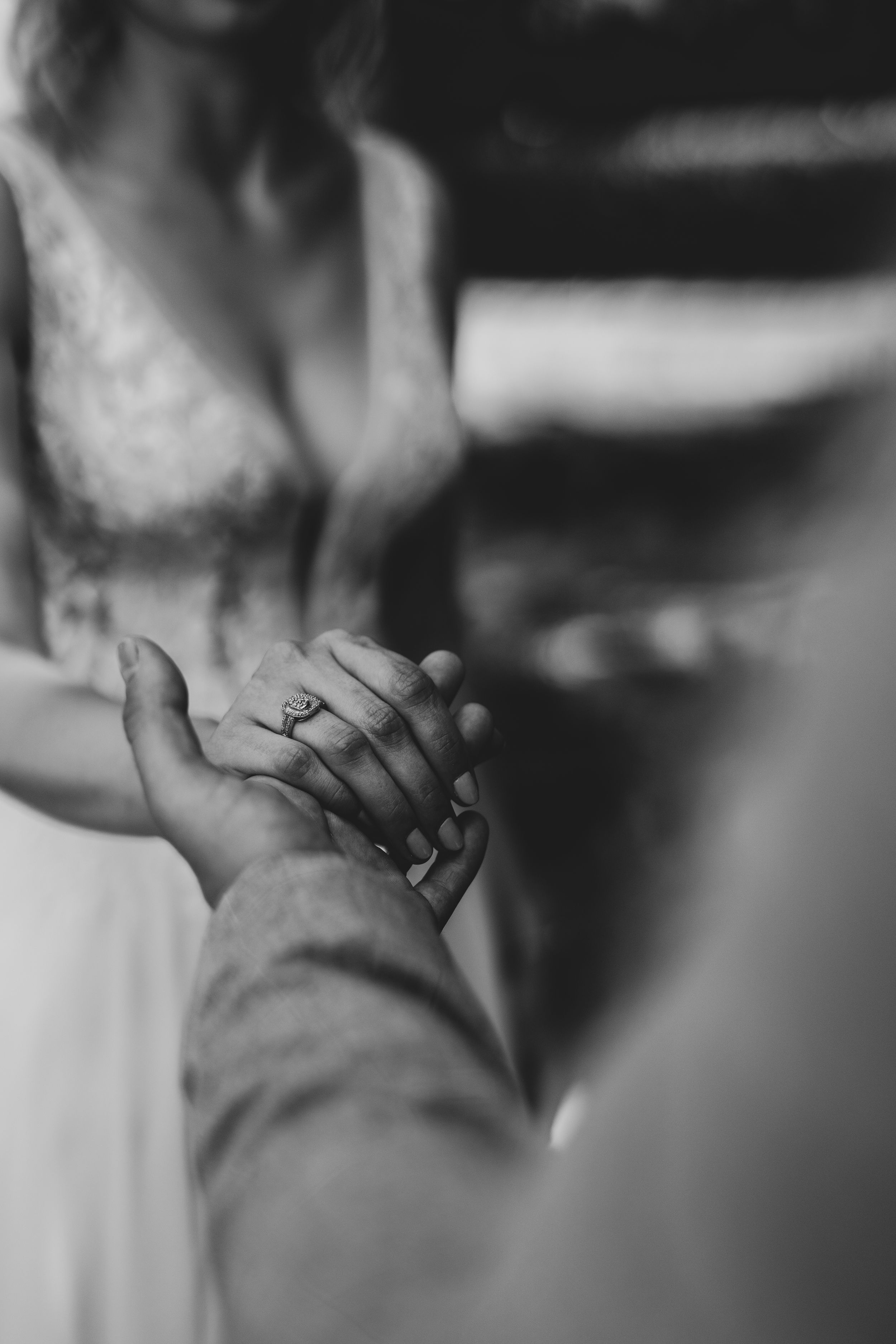 Black and white close-up of intertwined hands with wedding rings.