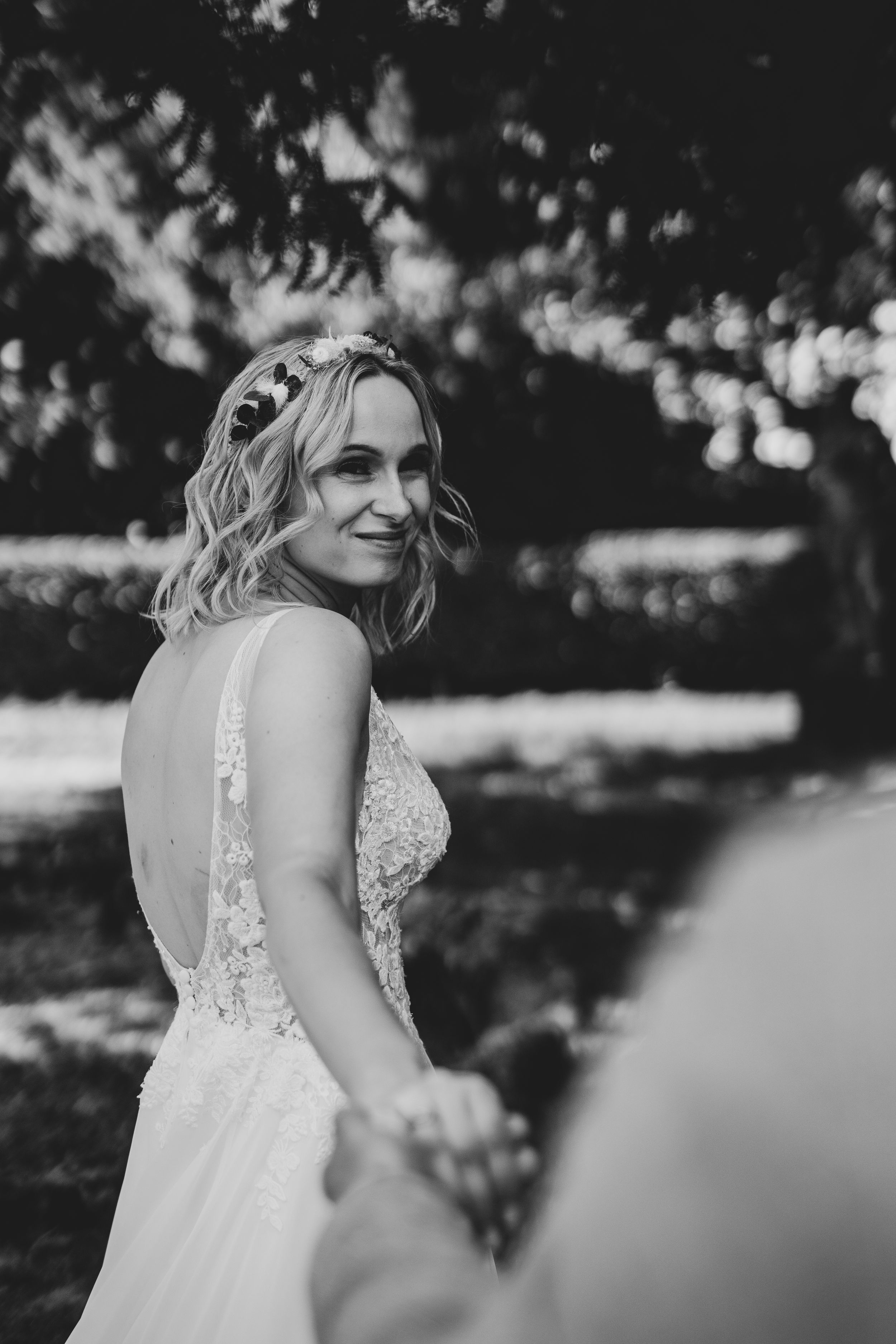 Bride in a lace wedding dress smiling outdoors with bokeh lighting.