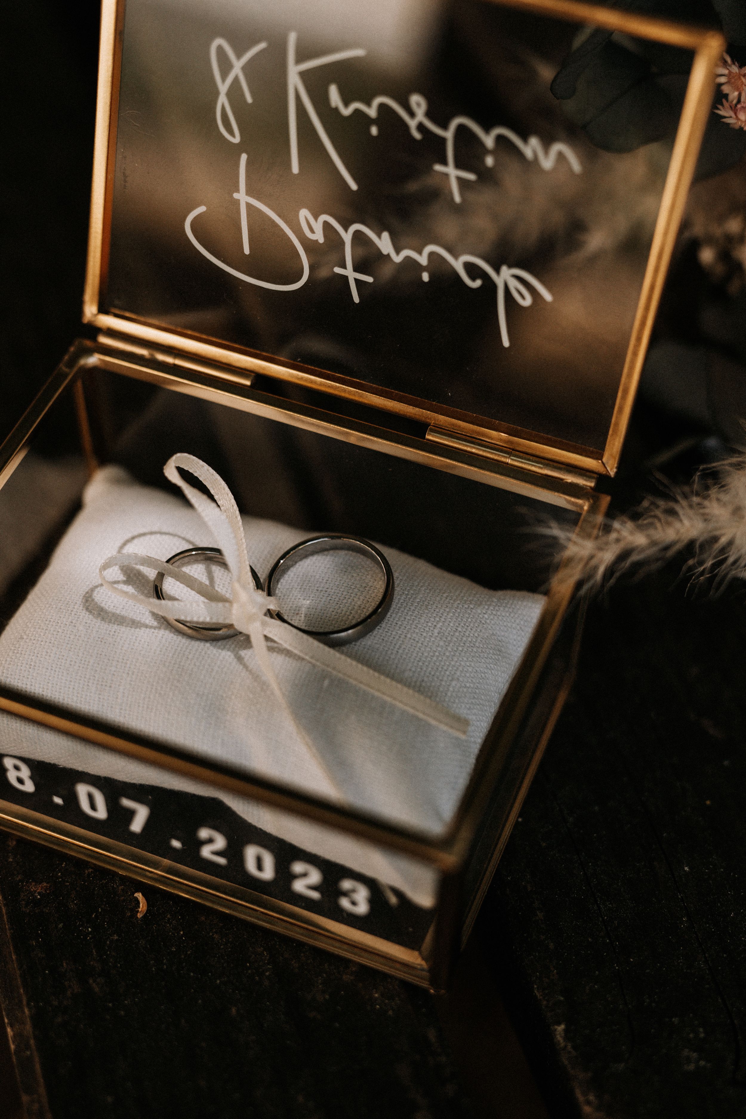 Wedding rings tied with white ribbon in gold glass box with date inscription.