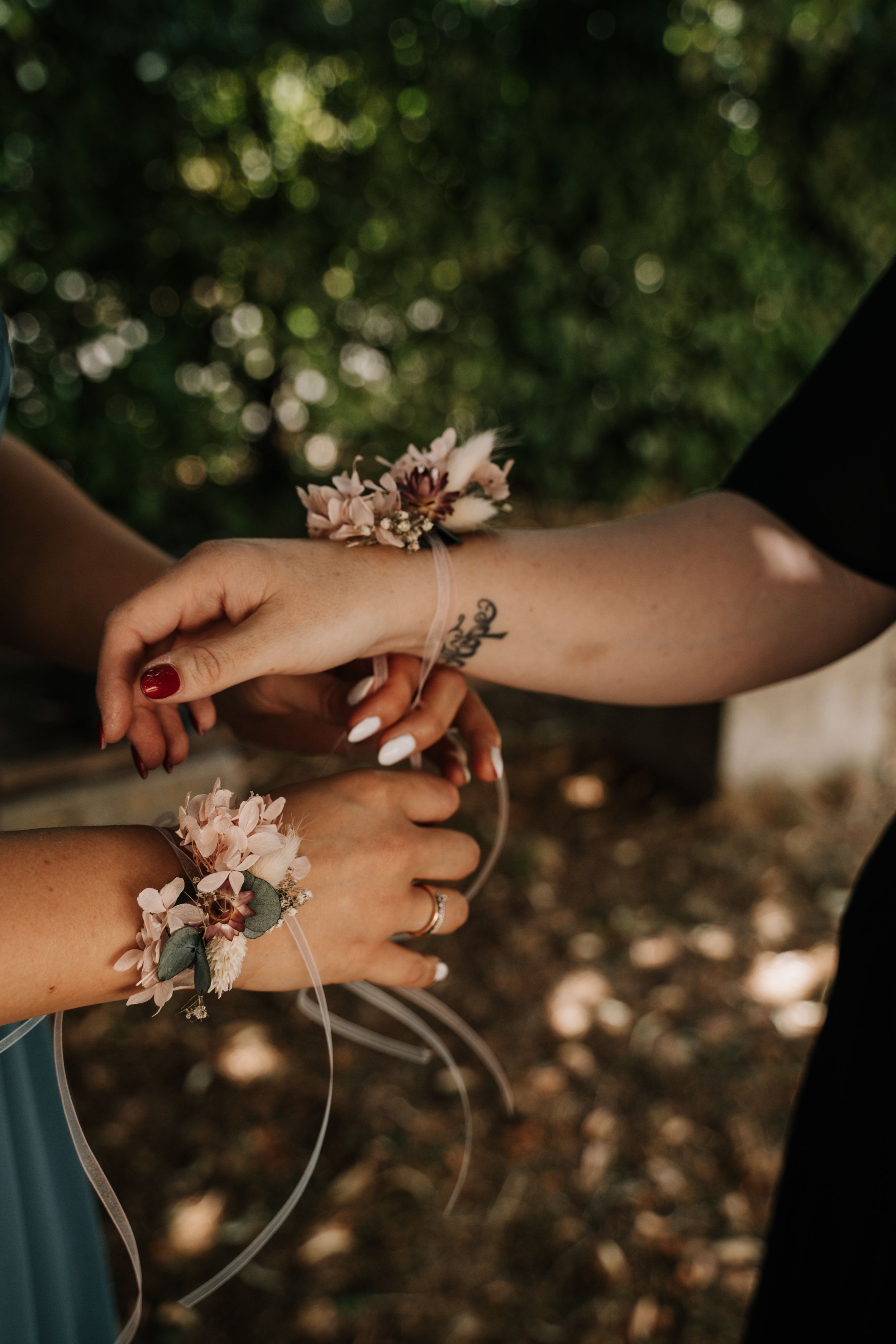 Hands wearing delicate floral corsages in natural outdoor lighting.