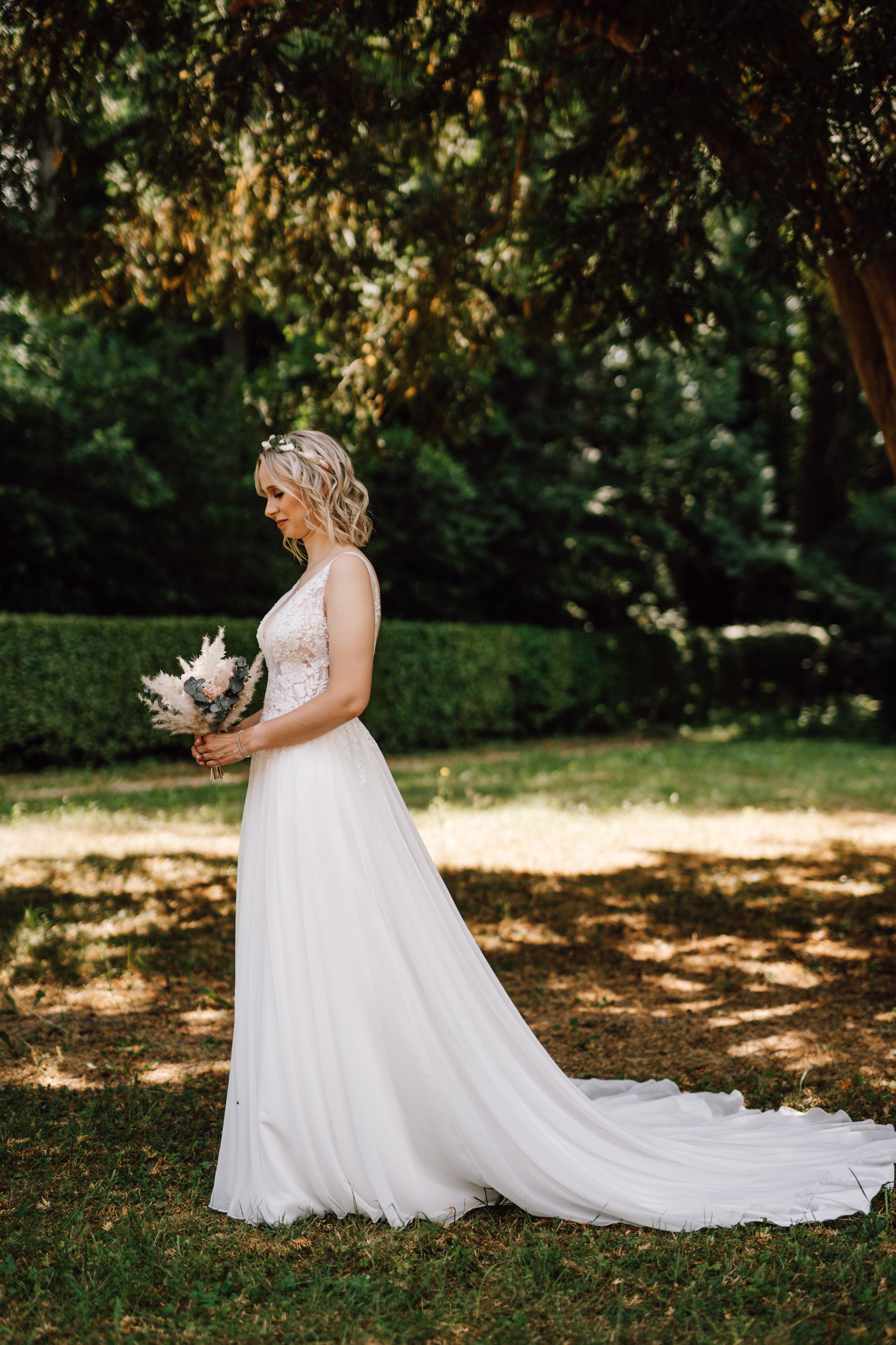 Elegant bride in flowing white lace gown poses in a garden setting with trailing train.