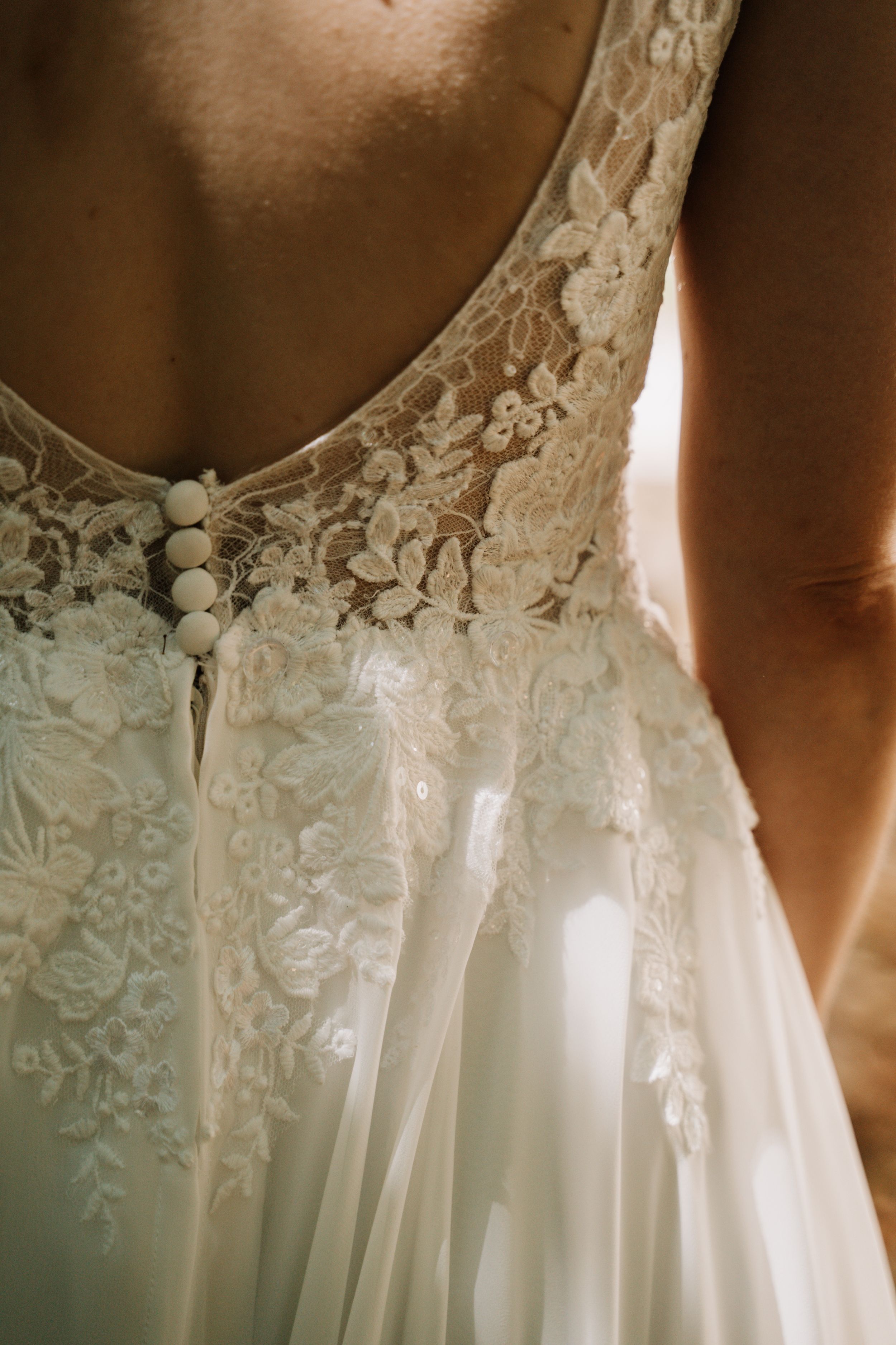 Detail shot of intricate lace and button details on white wedding dress.