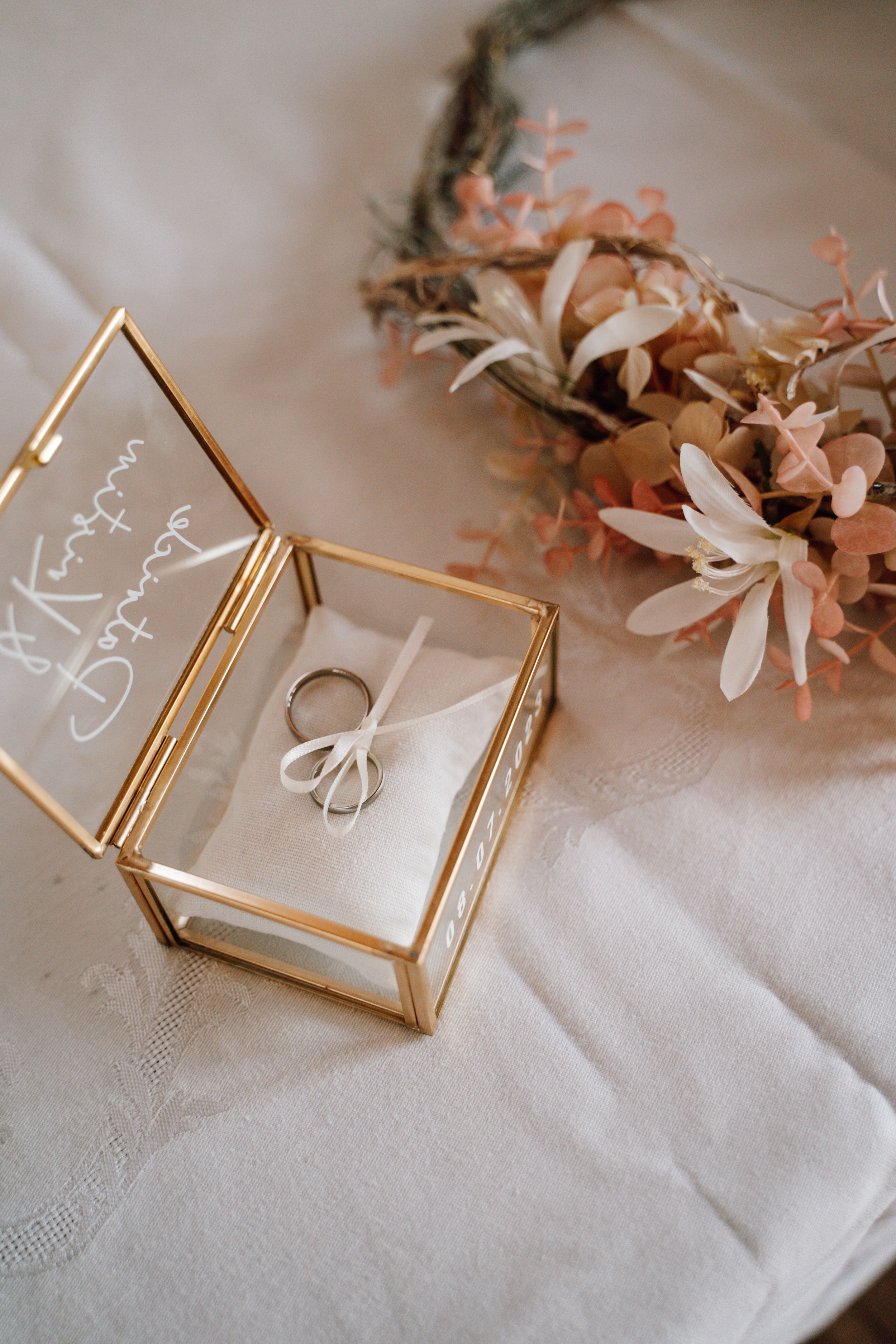 Delicate gold wedding rings displayed with soft pink flowers and white lace on a light fabric background.
