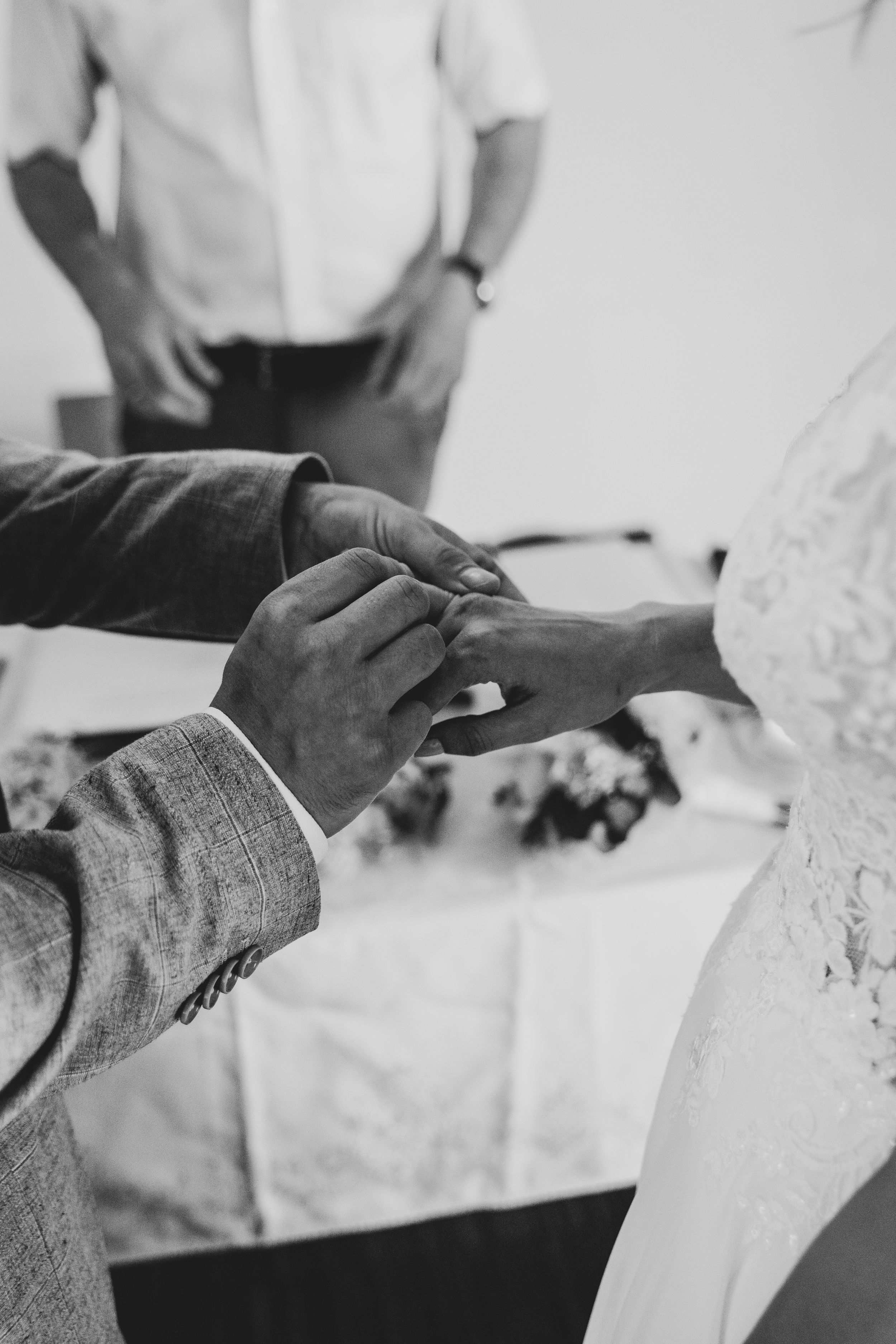 Black and white close-up of hands exchanging rings during a wedding ceremony.