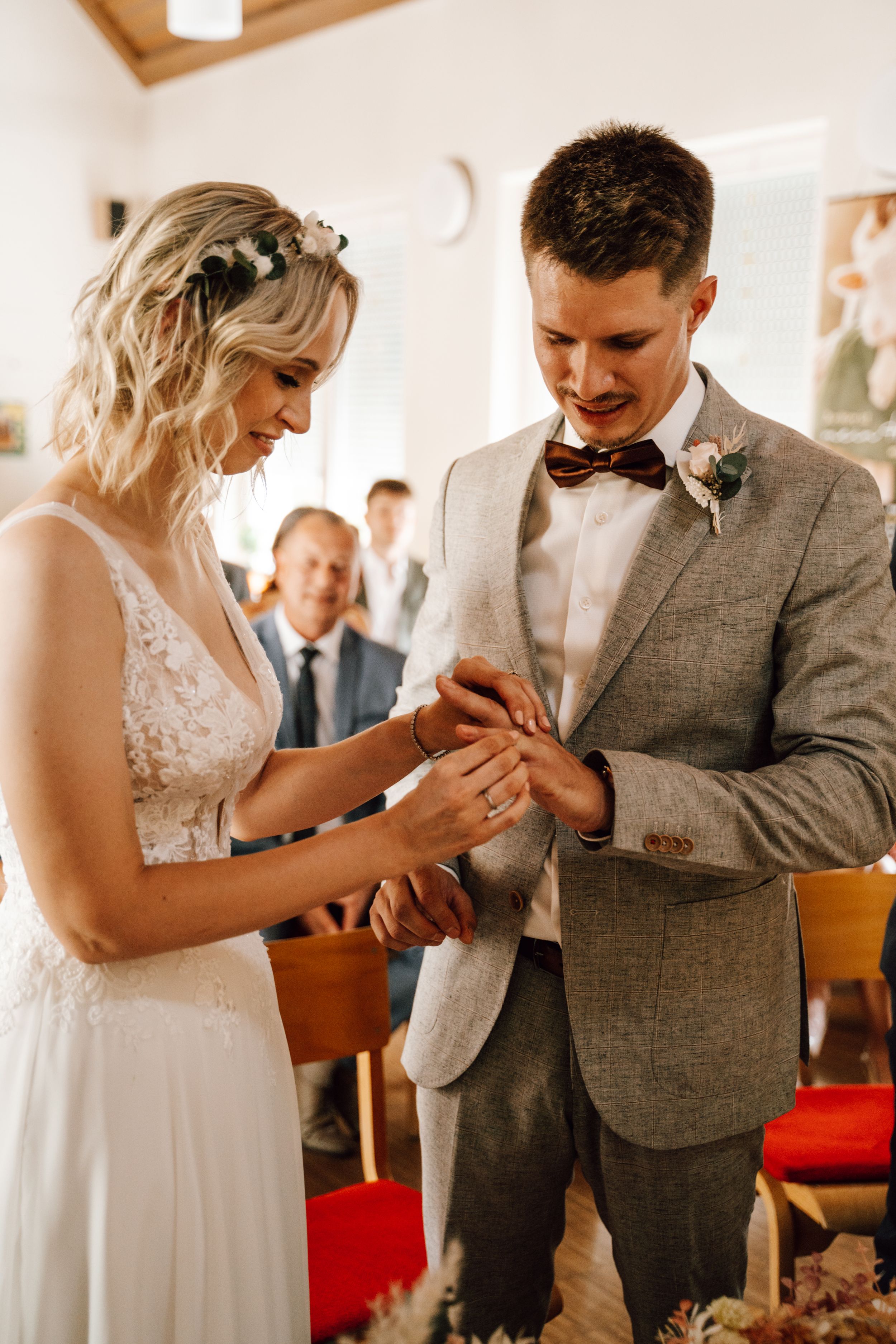 Couple in wedding attire exchanging rings during intimate indoor ceremony.