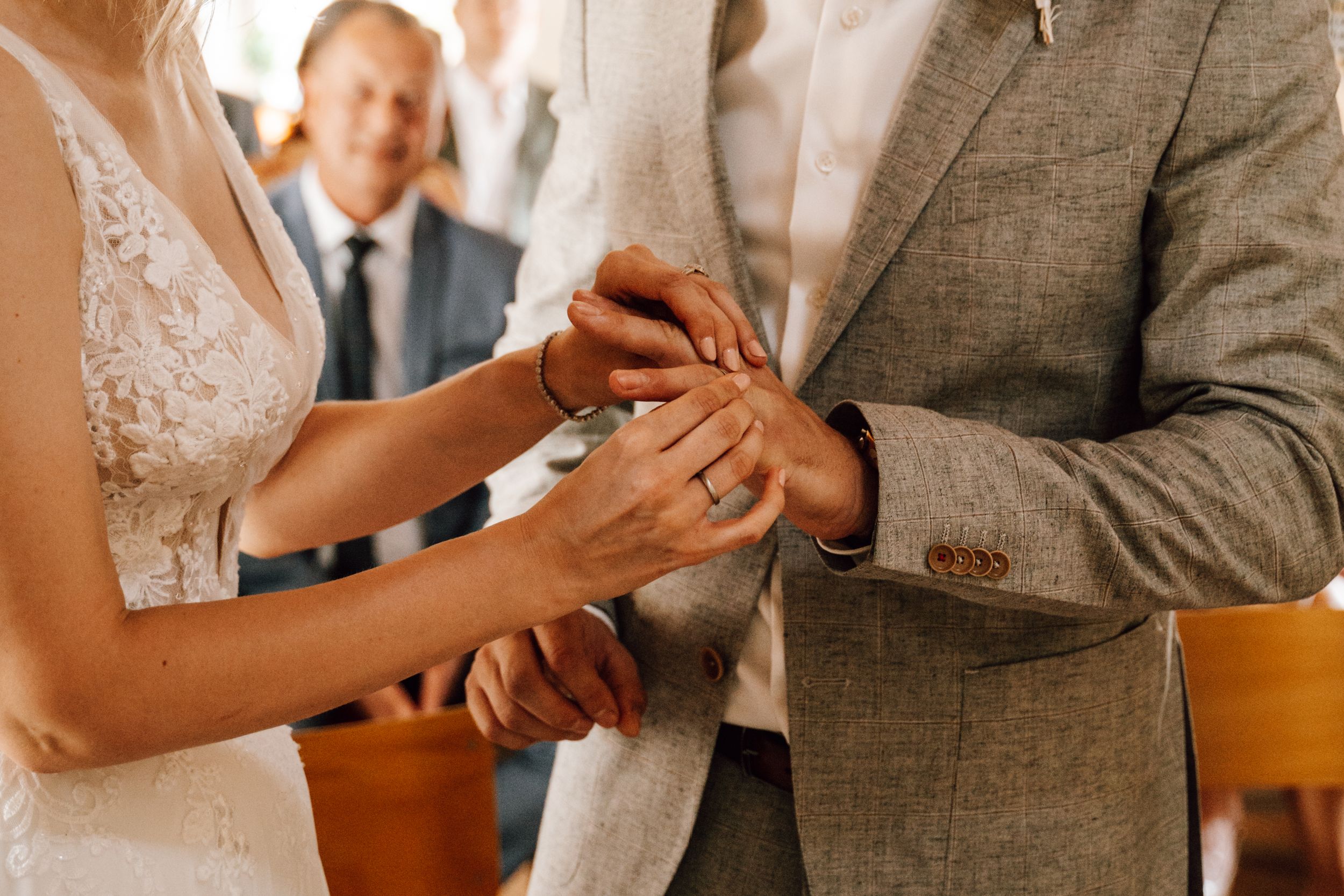 Wedding couple's hands during ring exchange ceremony in warm lighting.