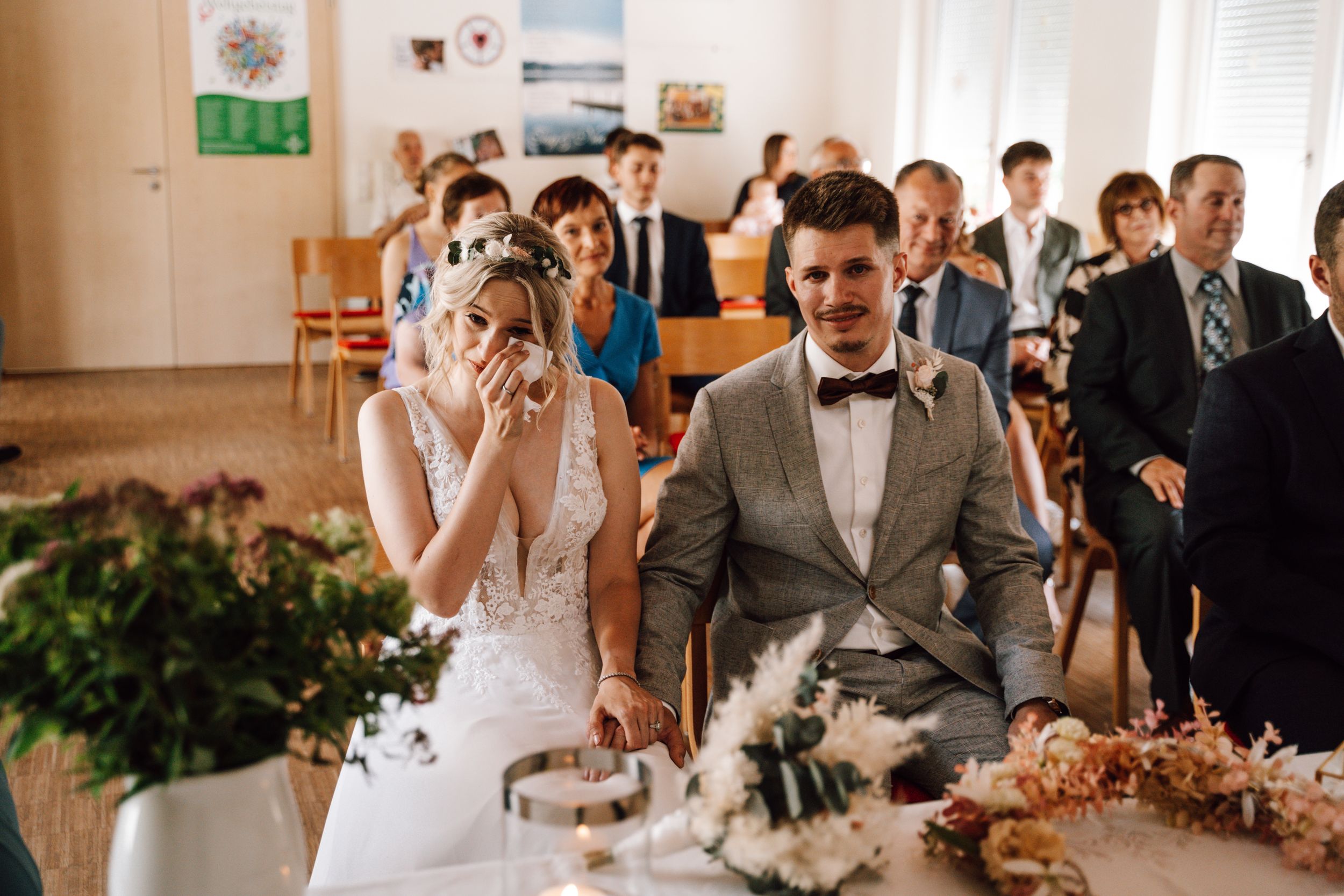 Wedding ceremony in bright indoor venue with decorative floral arrangements.