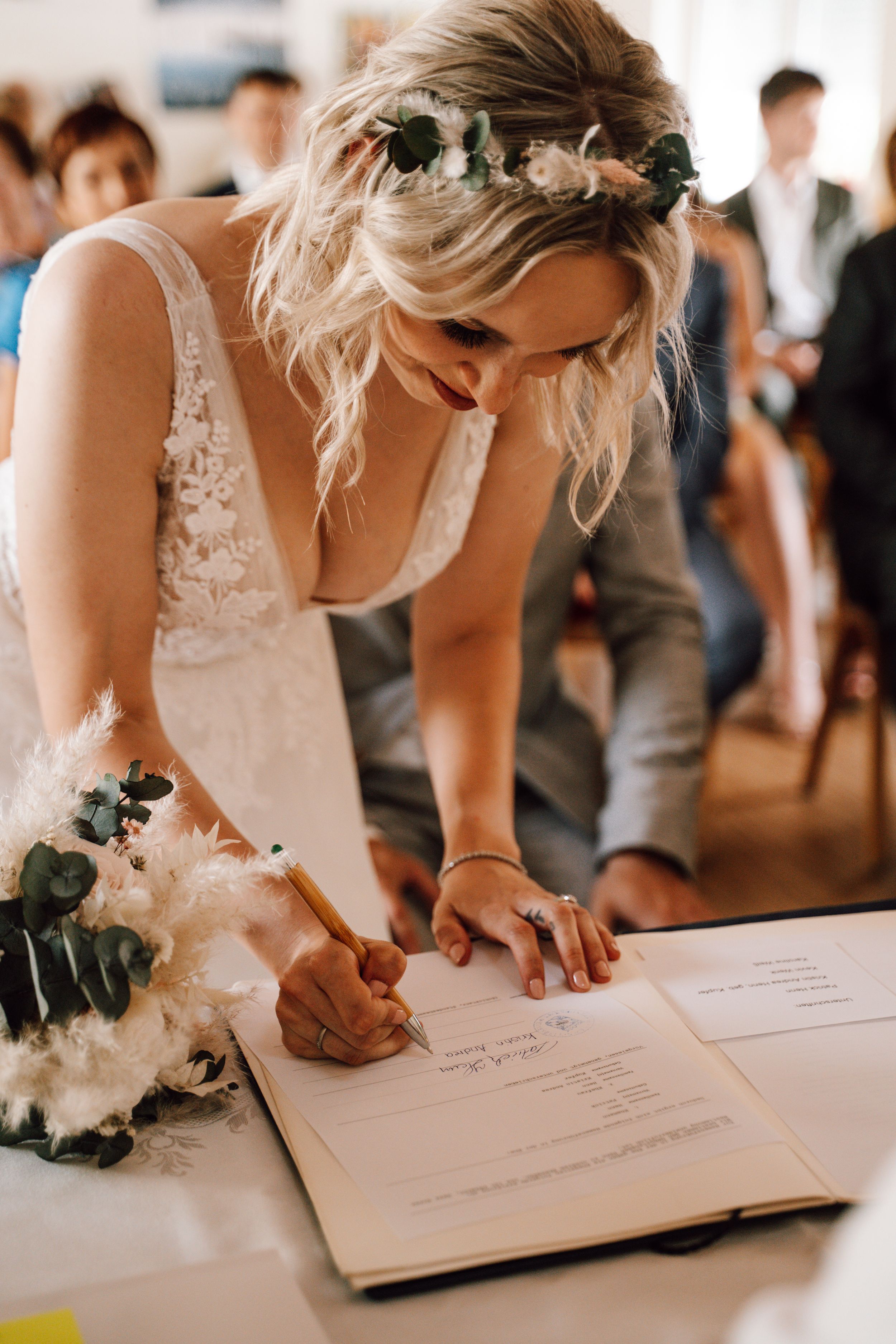Bride signing marriage certificate with floral decorations on table.