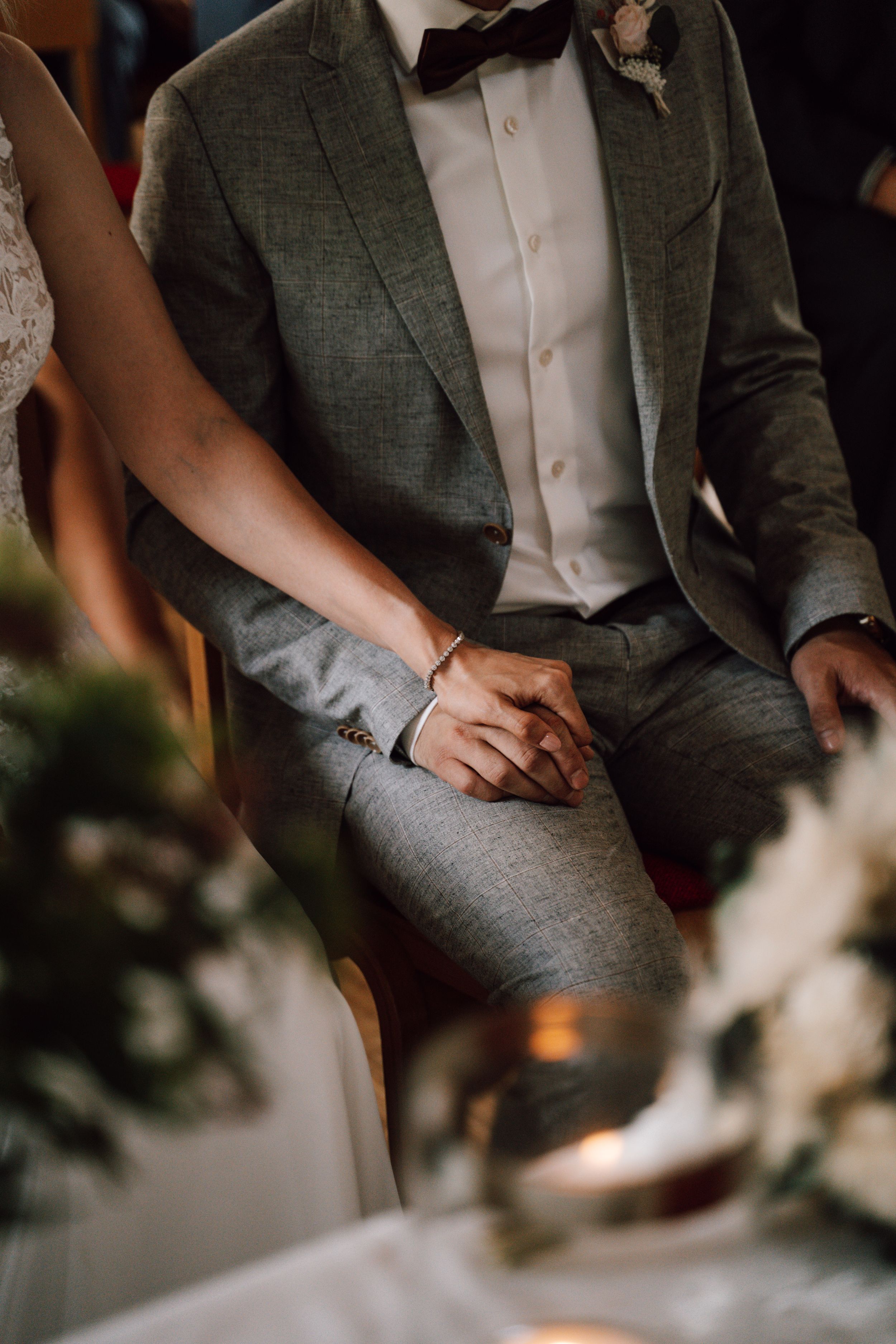 Close-up of a groom in a dark green suit and bowtie sitting during a wedding celebration.