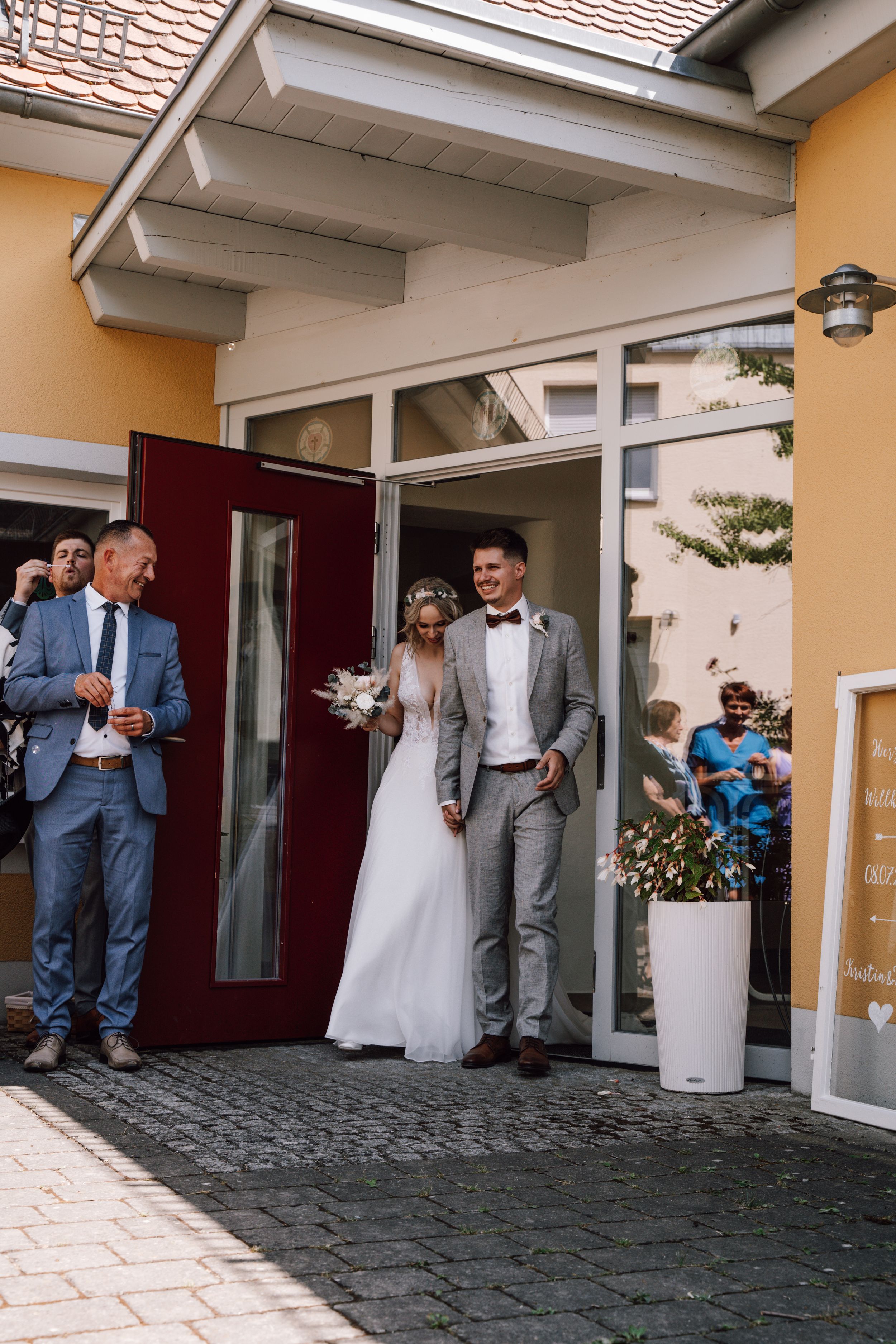 Wedding couple exiting a building entrance with orange walls and red door.
