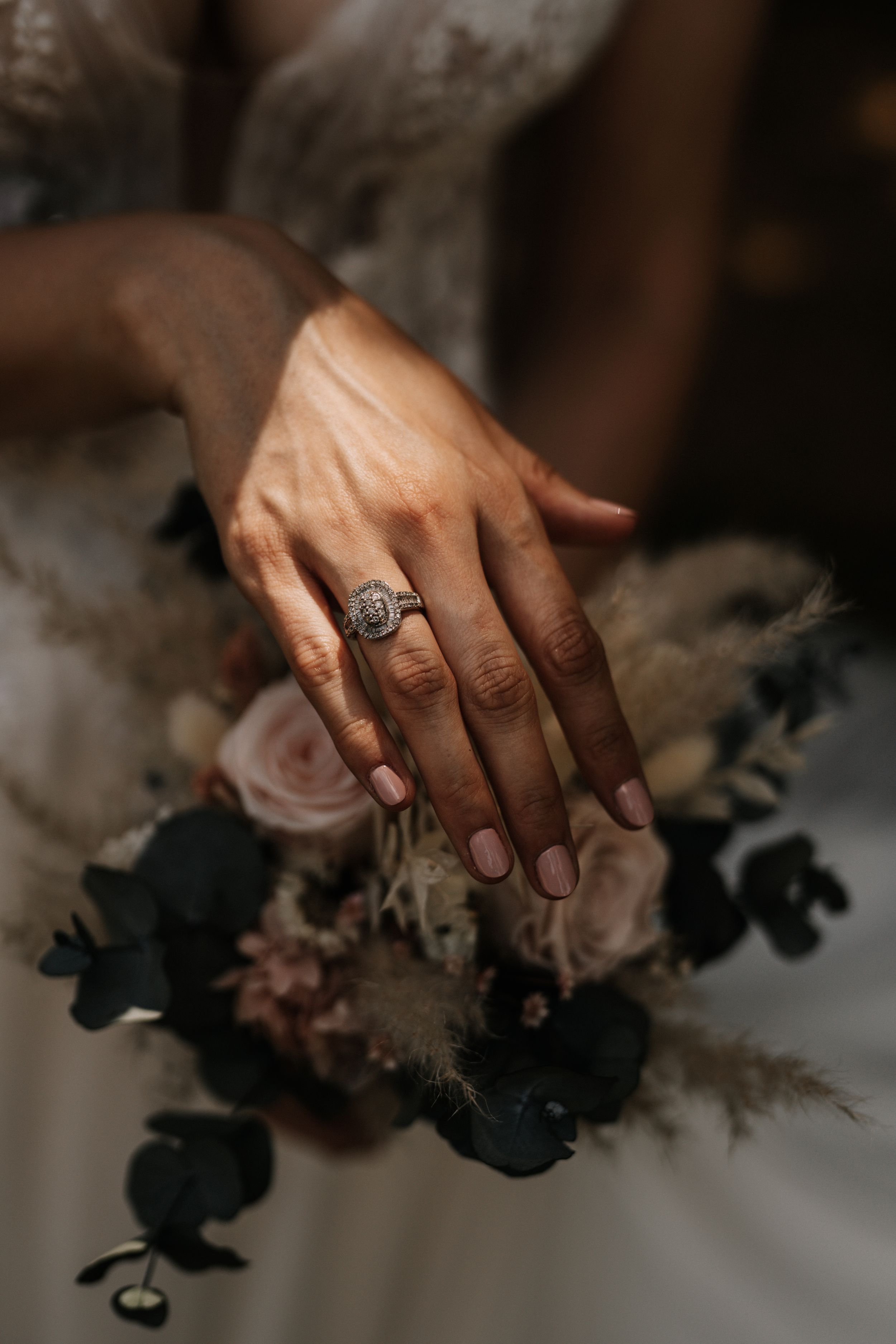 Detail shot of hands holding wedding bouquet with engagement ring visible.