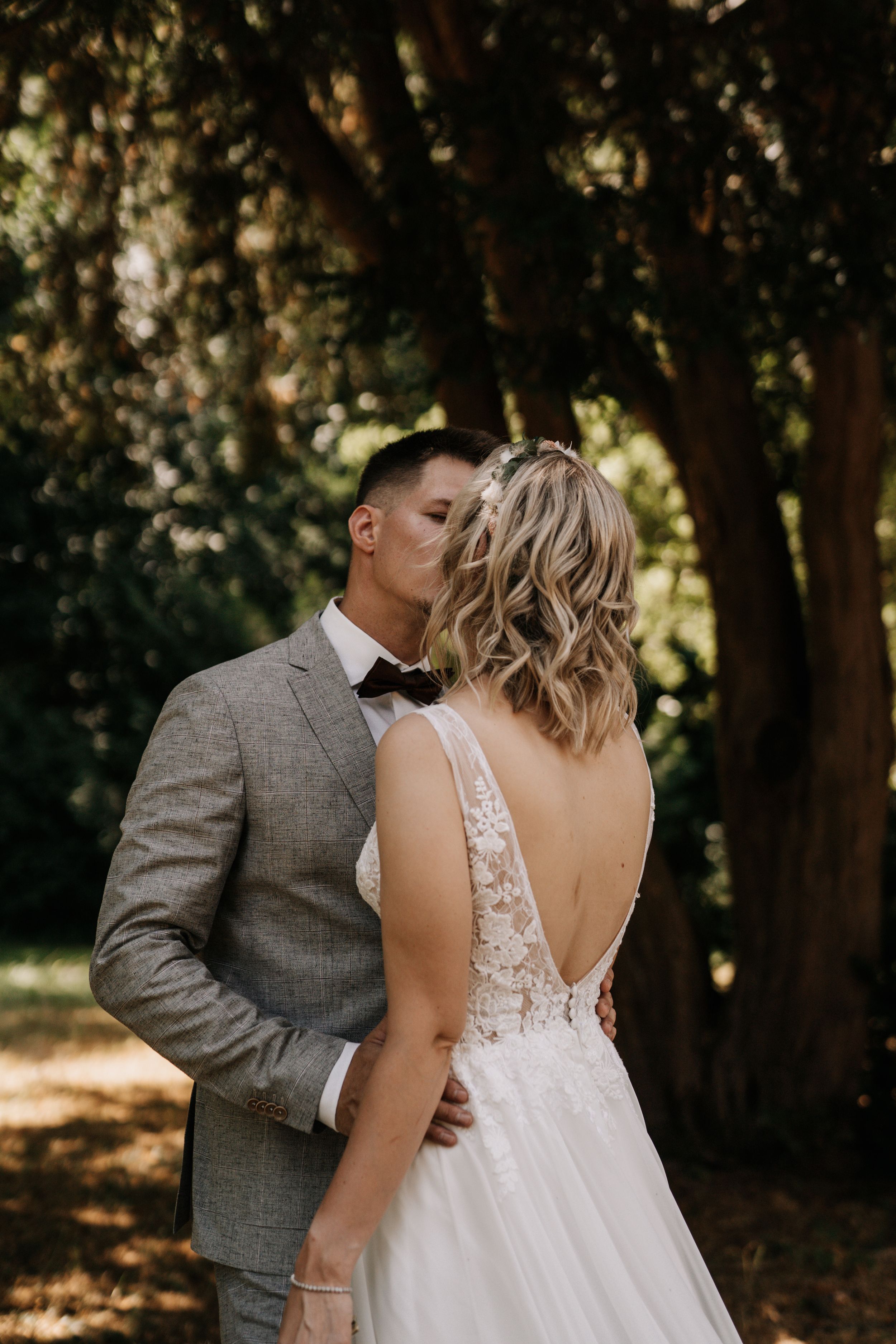 Romantic wedding couple embraces in a sunlit forest setting.
