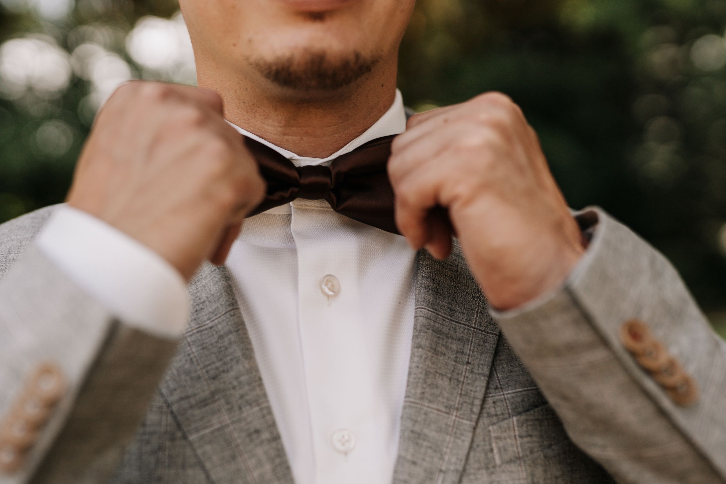 Groom adjusts his collar and tie in a candid wedding day moment.