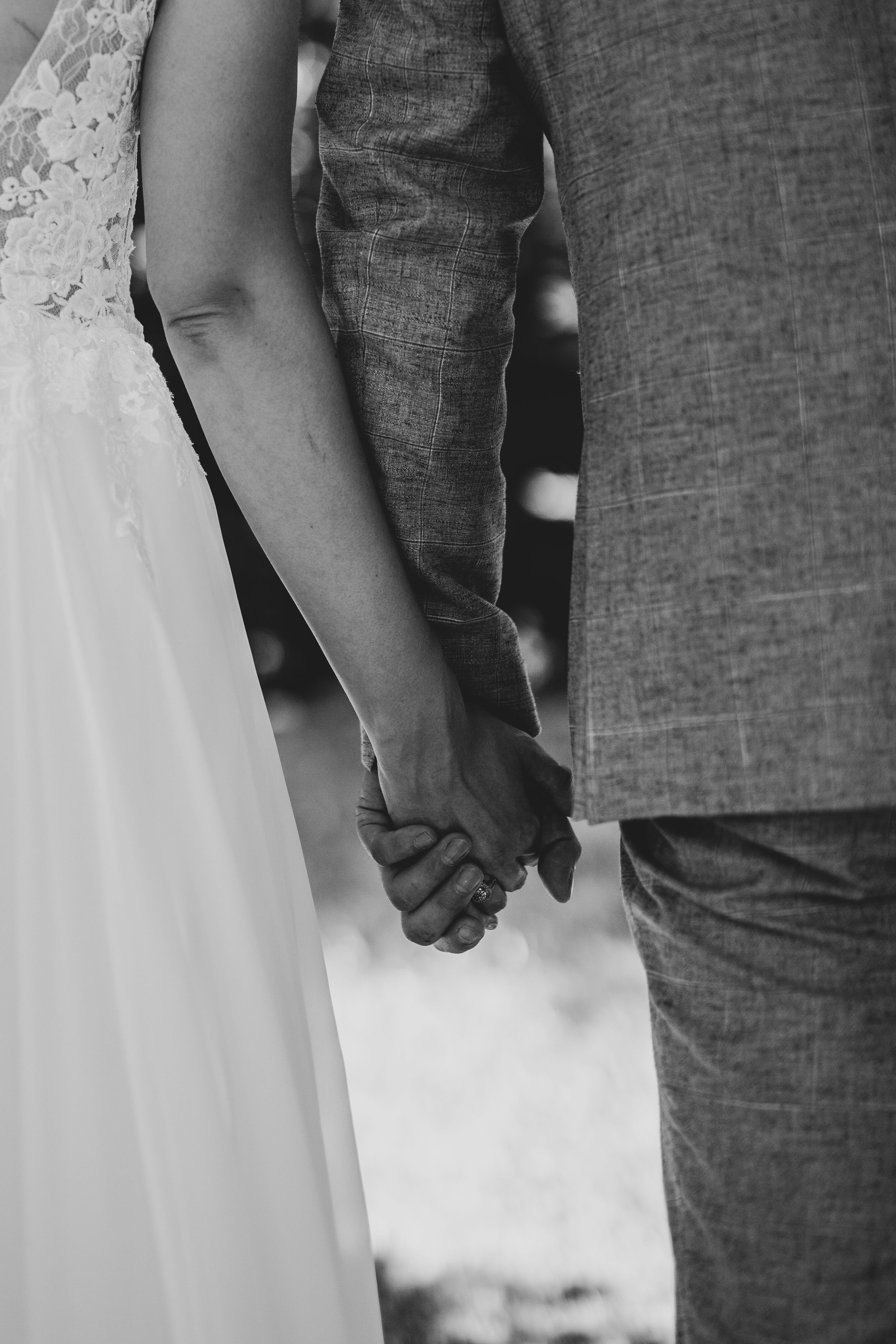 Black and white close-up of newlyweds holding hands, showing dress and suit details.