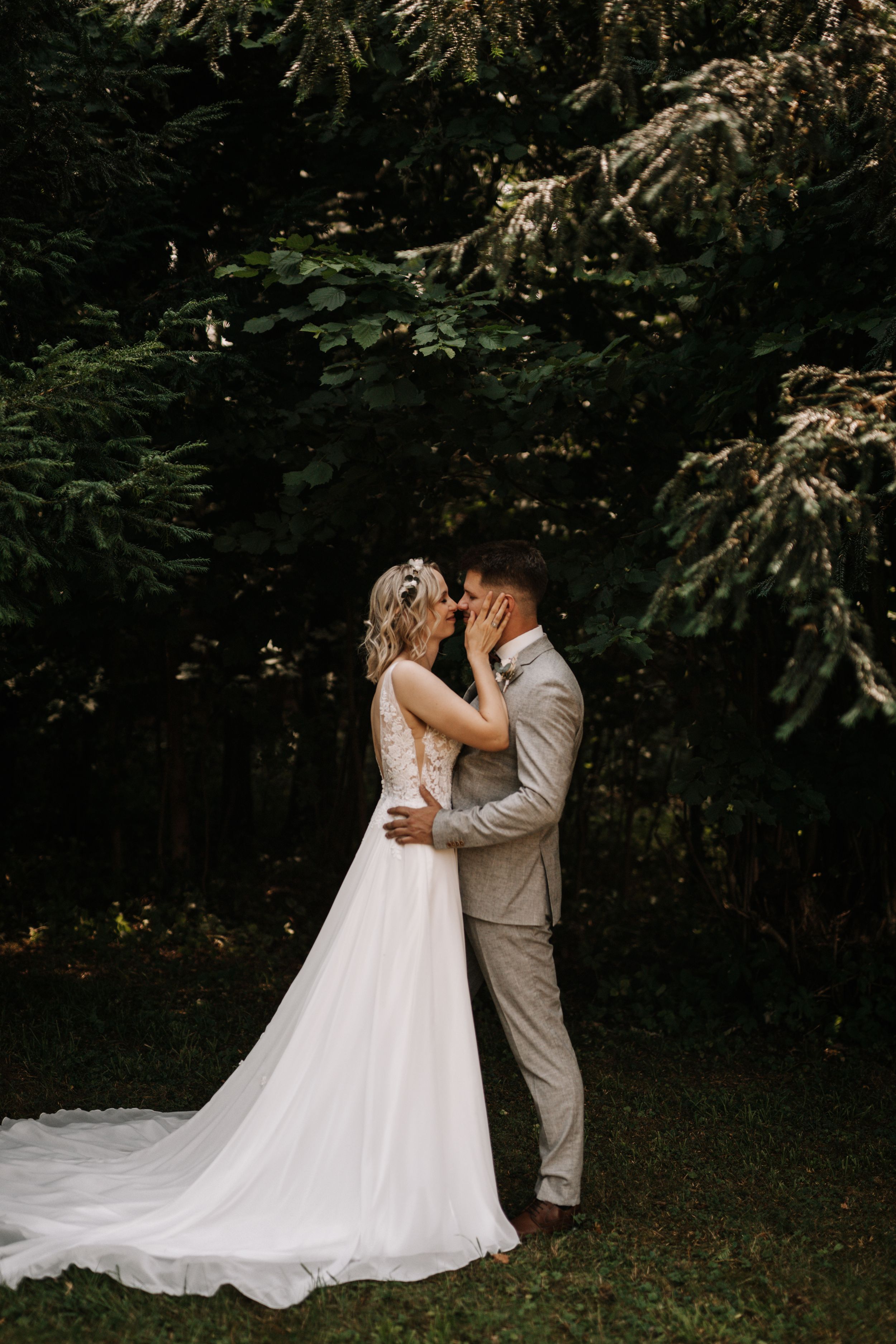 A tender wedding moment captured in a wooded setting with flowing white dress.