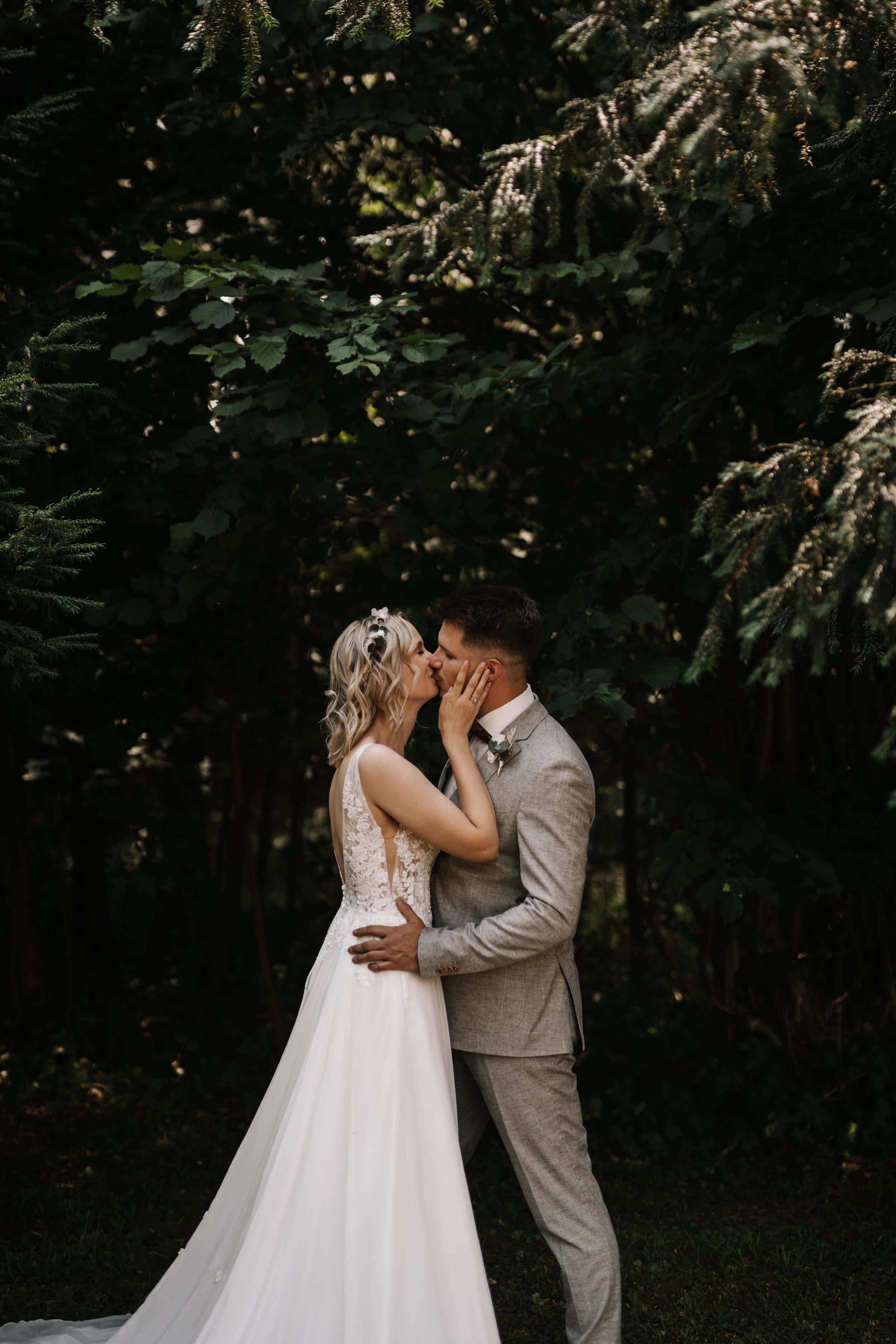 A romantic wedding kiss in a forest setting with natural greenery backdrop.