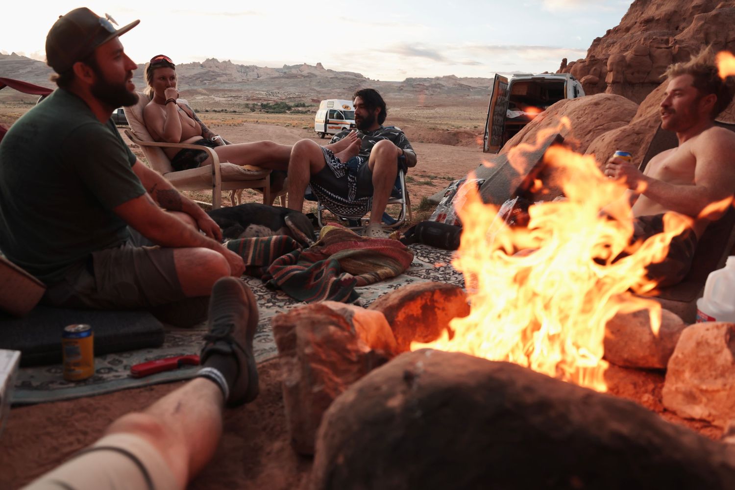 Group gathered around large bonfire on desert rocks at sunset.