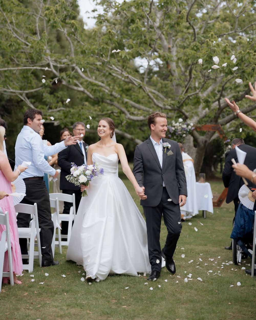 A joyful wedding ceremony exit where guests toss flower petals as the newlyweds walk down an outdoor aisle together.