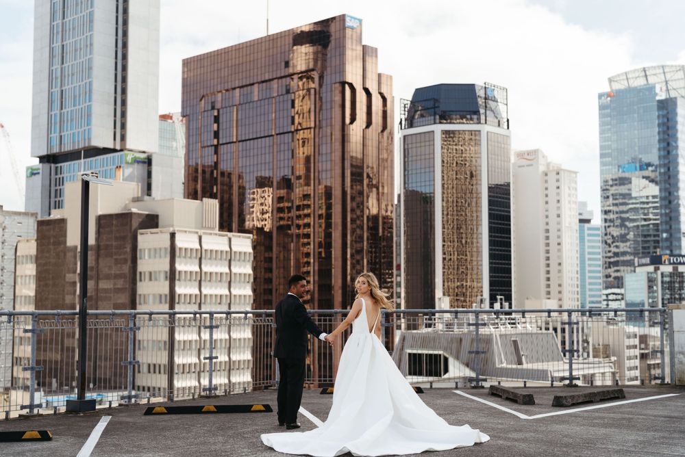 Wedding couple poses on urban rooftop with modern city skyline backdrop.