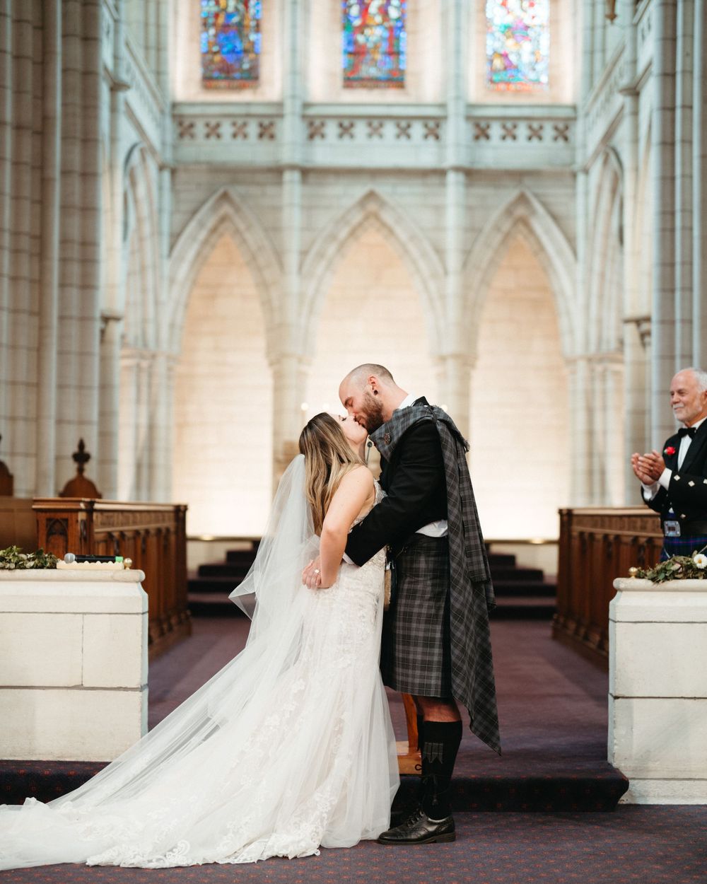 Romantic wedding kiss in a cathedral with dramatic gothic architecture and stained glass windows.