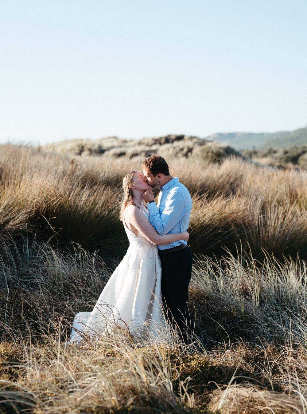 A couple shares an intimate moment in tall grass during a golden hour wedding photo session in a rural landscape.