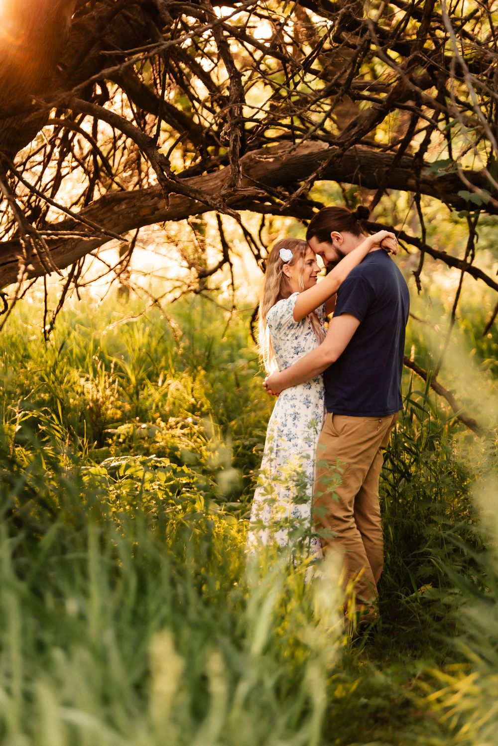 A romantic moment beneath tree branches during golden hour in a natural setting.
