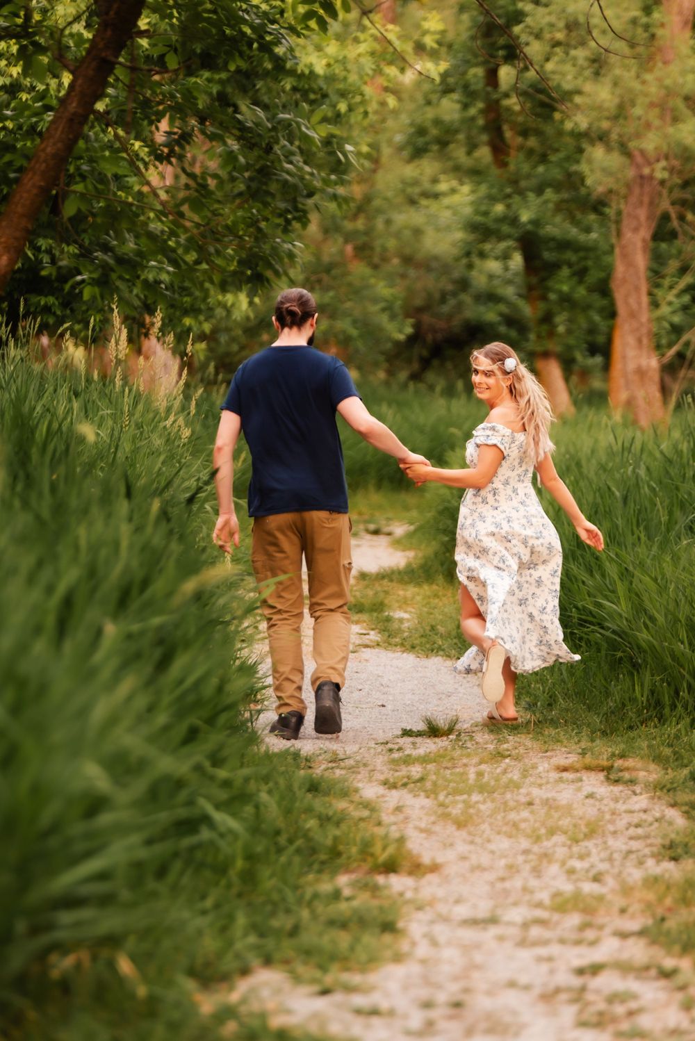 A couple walks hand in hand down a winding path through lush summer greenery.