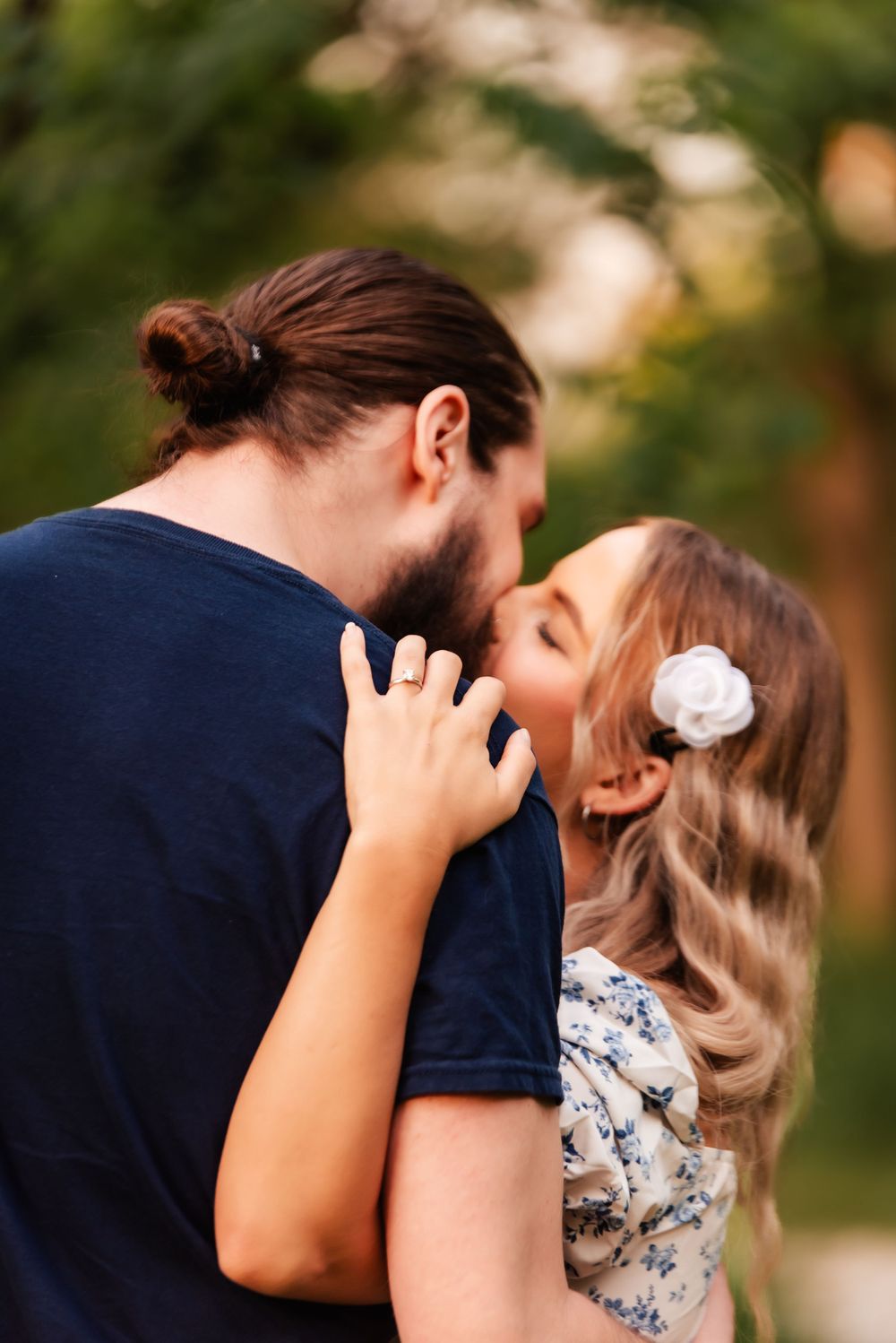 A romantic embrace captured in soft natural lighting with a delicate white flower accent.