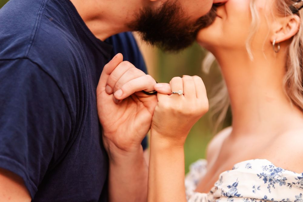 An intimate closeup of two people holding hands with engagement rings visible.