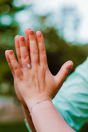 A close-up shot of a hand showing off an engagement ring against a blurred natural background.