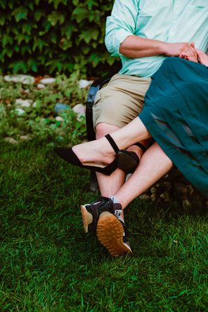Legs in khaki shorts and a mint shirt sit cross-legged on grass wearing hiking boots near ivy-covered wall.