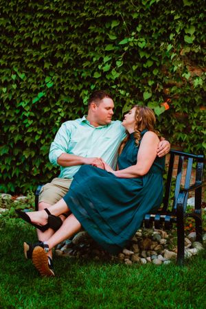 A romantic couple shares a tender moment on a garden bench surrounded by lush green ivy wall.