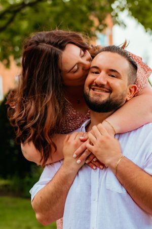 A couple embraces outdoors on a sunny day, sharing an affectionate moment with a tender kiss and warm smiles.
