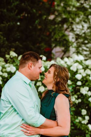 A romantic couple share an intimate moment in front of blooming white flowers in a garden setting.