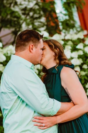 A romantic outdoor engagement photo of a couple wearing mint and emerald colors embracing among foliage.