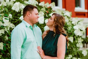 A couple shares a romantic moment in front of blooming white hydrangeas and an orange wall.