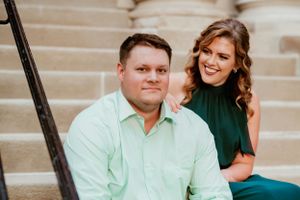 A couple sits together on outdoor concrete steps with the woman in a green top and the man in a mint colored shirt.