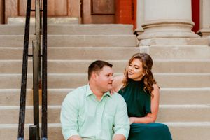 A couple sits together on outdoor stone steps, with one person wearing mint green and the other in an emerald dress.