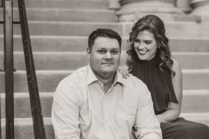 Black and white photo of a couple posing together on stone steps with architectural details in the background.