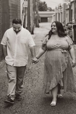 A couple walks hand in hand down an alley as they share a happy moment together in black and white photography.