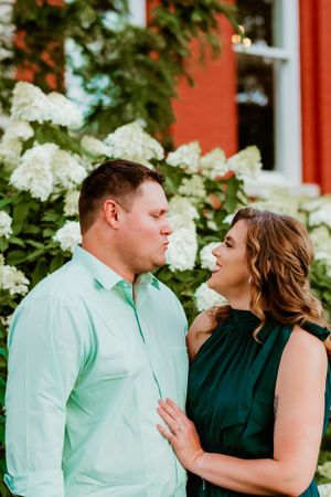 A couple in mint green and forest green attire pose together against a backdrop of hydrangeas and red walls.