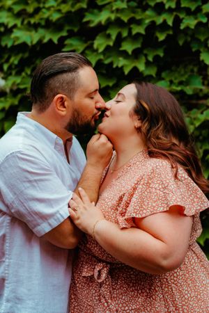 A romantic couple share an intimate moment in front of a leafy green ivy wall backdrop, with soft natural lighting.