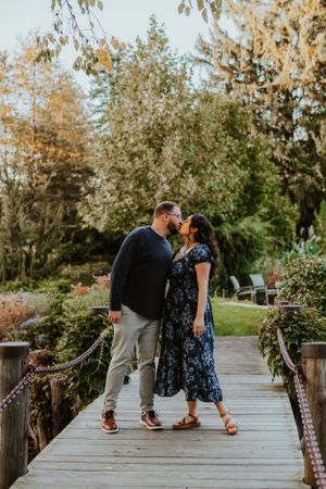A couple shares an intimate moment while standing on a wooden bridge surrounded by autumn foliage at sunset.